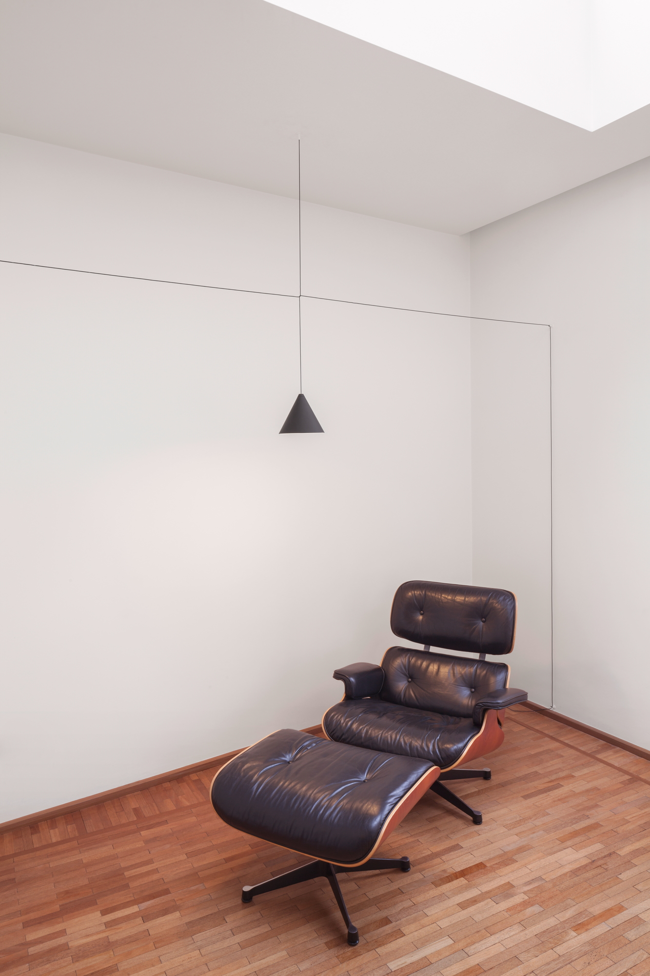 Minimalistische Raumgestaltung mit Flos String Light Kegelkopf Pendelleuchte über Ledersessel. Design Lampe für Wohnzimmer.