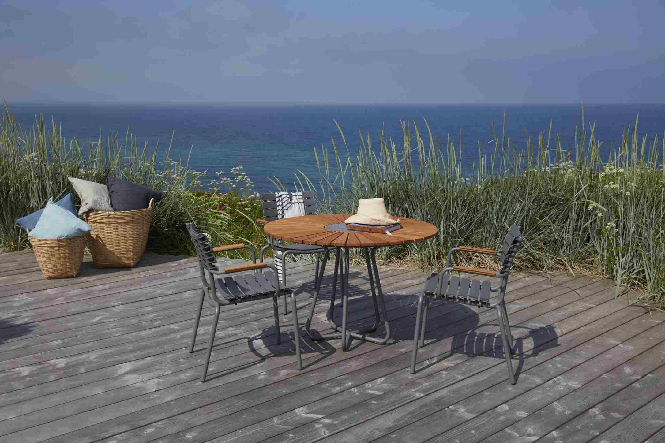 Houe Circle Gartentisch Ø 110 cm aus Bambus mit grauen Stühlen auf Holzterrasse am Meer.