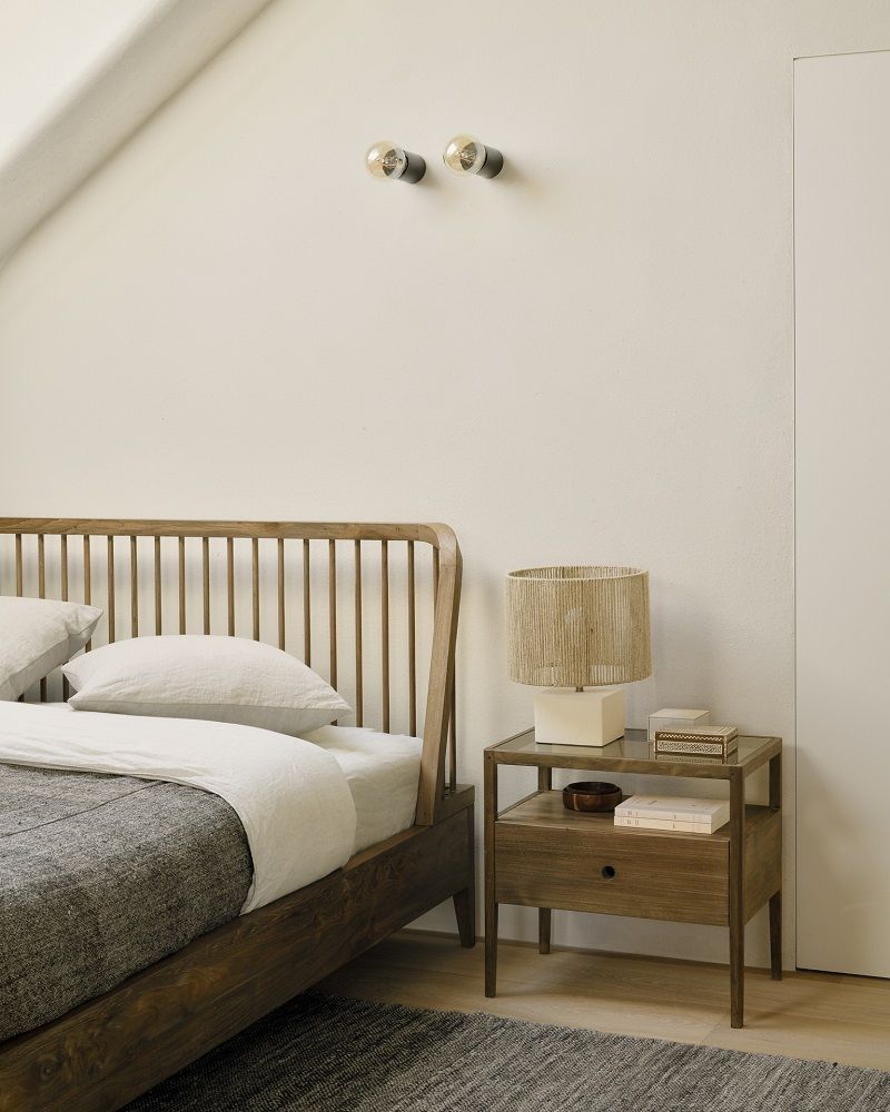 Spindle Nachttisch von Ethnicraft aus Teakholz mit Schublade neben einem Bett mit Lampe.