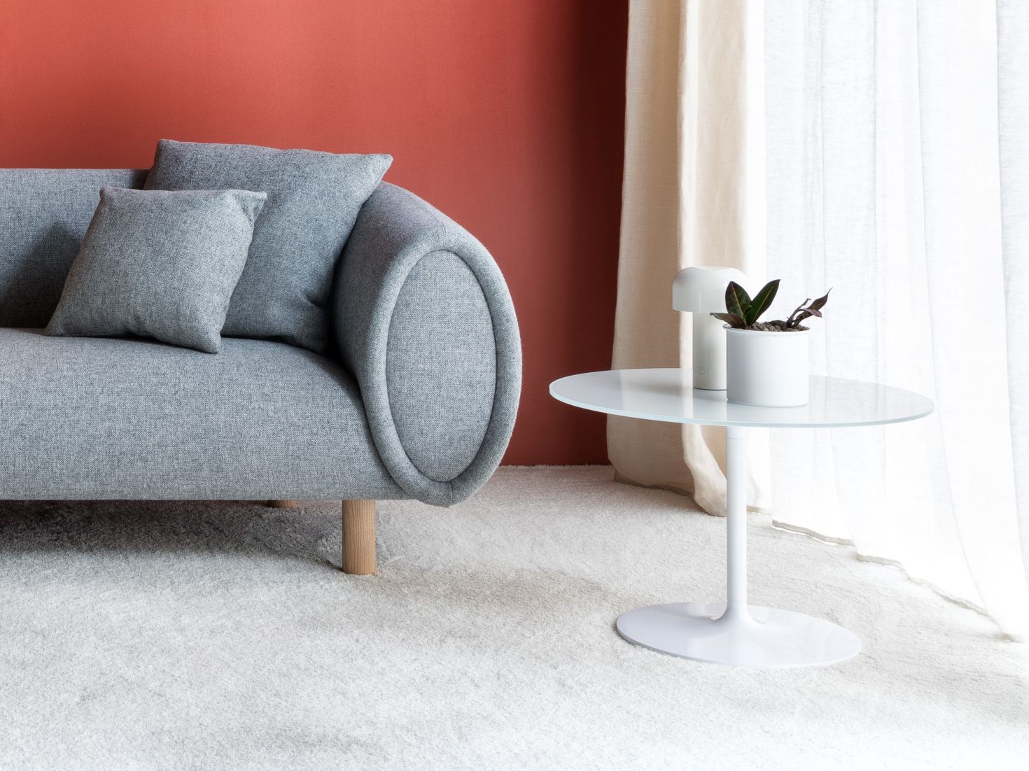 Weißer Poppy Beistelltisch mit Glasplatte neben grauem Sofa und Zimmerpflanze. Moderner Beistelltisch für Wohnzimmer.