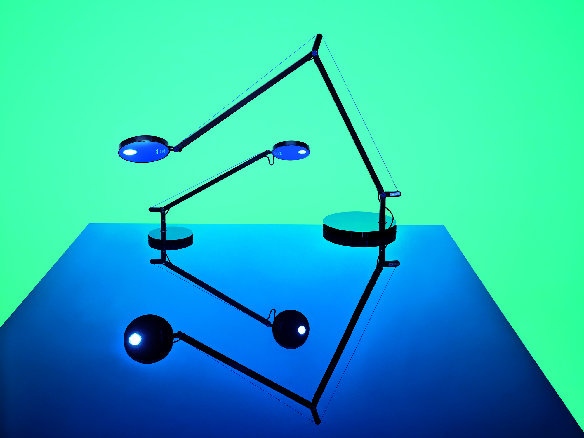 Drei schwarze Demetra Tischleuchten von Artemide mit LED-Licht auf blauem Untergrund.