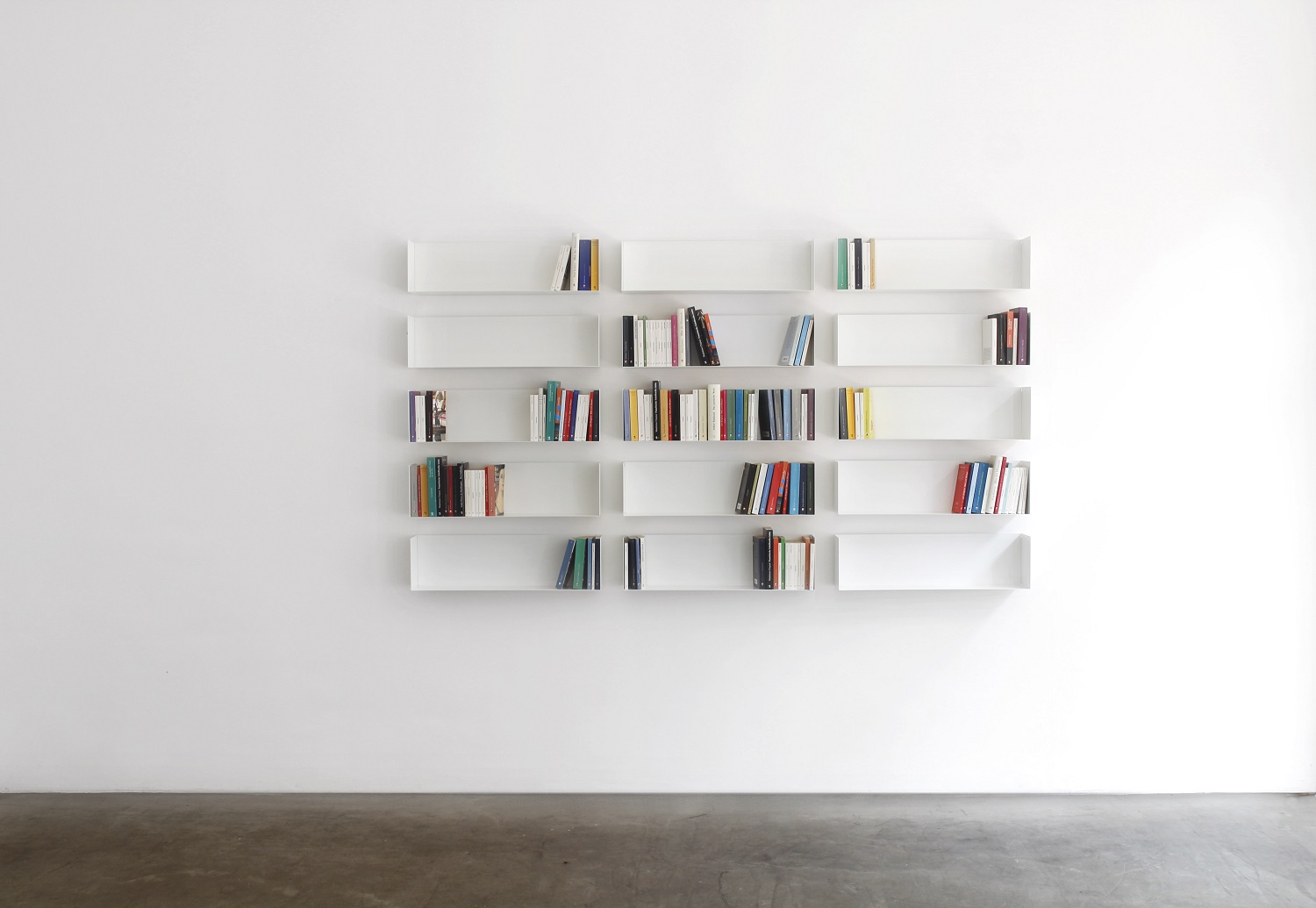 Weißes Taschenbuchregal a Linea1 von Müller Möbelwerkstätten an einer weißen Wand mit Büchern.