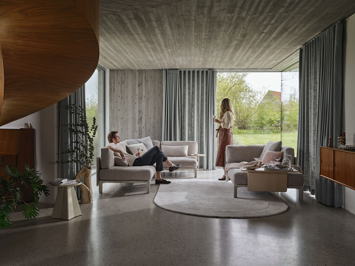 Helle Wohnzimmer-Szene mit Vitra Anagram Panel Sofa, zwei Personen und moderner Einrichtung.