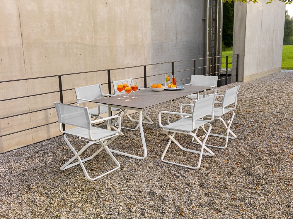 Ahoi Tisch Outdoor von Weishäupl mit sechs passenden Stühlen auf einem Kiesplatz.