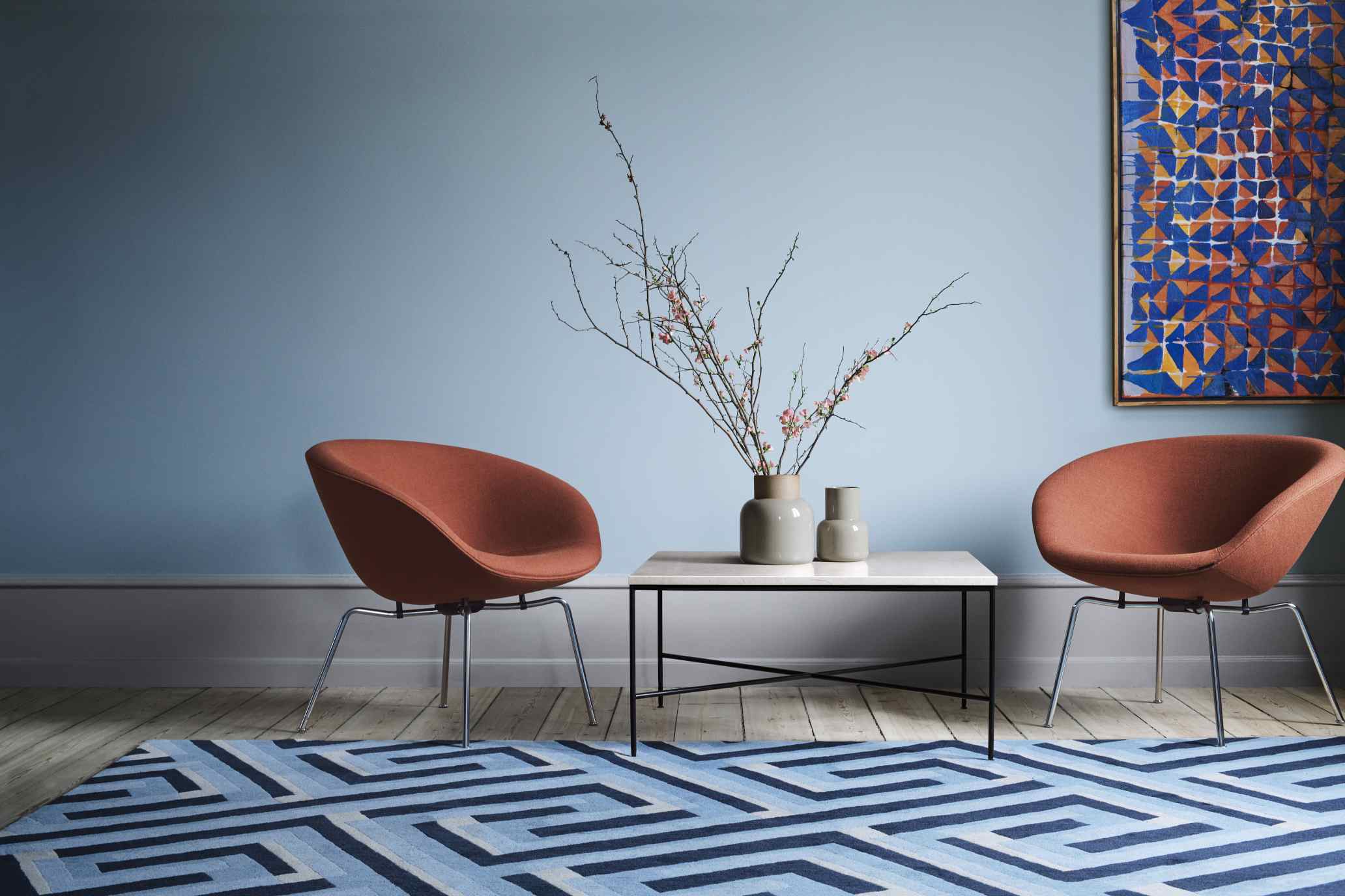 Zwei Fritz Hansen Pot Sessel in Terrakotta mit Couchtisch und blauem Teppich in modernem Wohnzimmer.