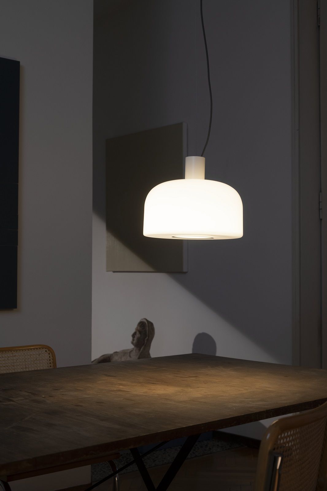 Nahaufnahme der Bellhop Glas Pendelleuchte von Flos über einem Esstisch.