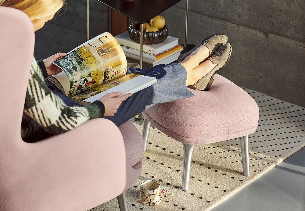 Frau liest im Sessel mit Füßen auf dem JH12 Fußhocker von Fritz Hansen in Rosa.