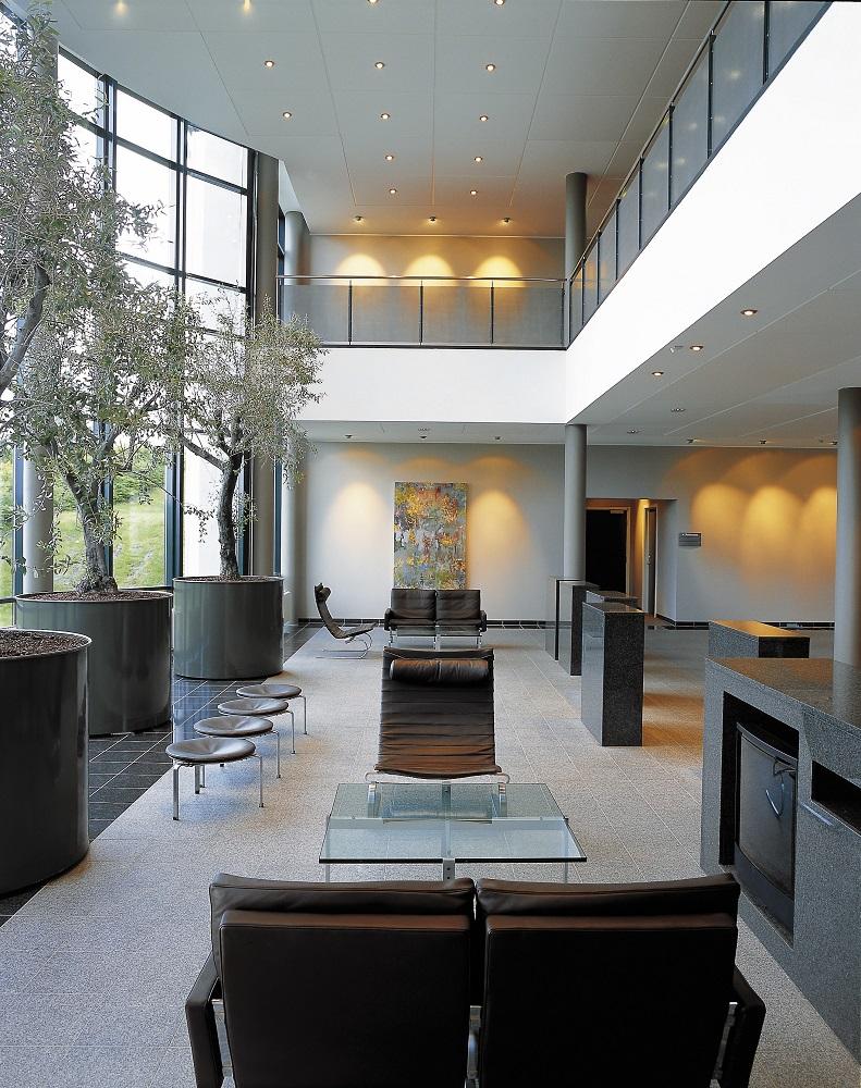 Innenaufnahme mit PK33 Hocker von Fritz Hansen, Ledersessel, Glascouchtisch und Olivenbäumen in Pflanzkübeln.