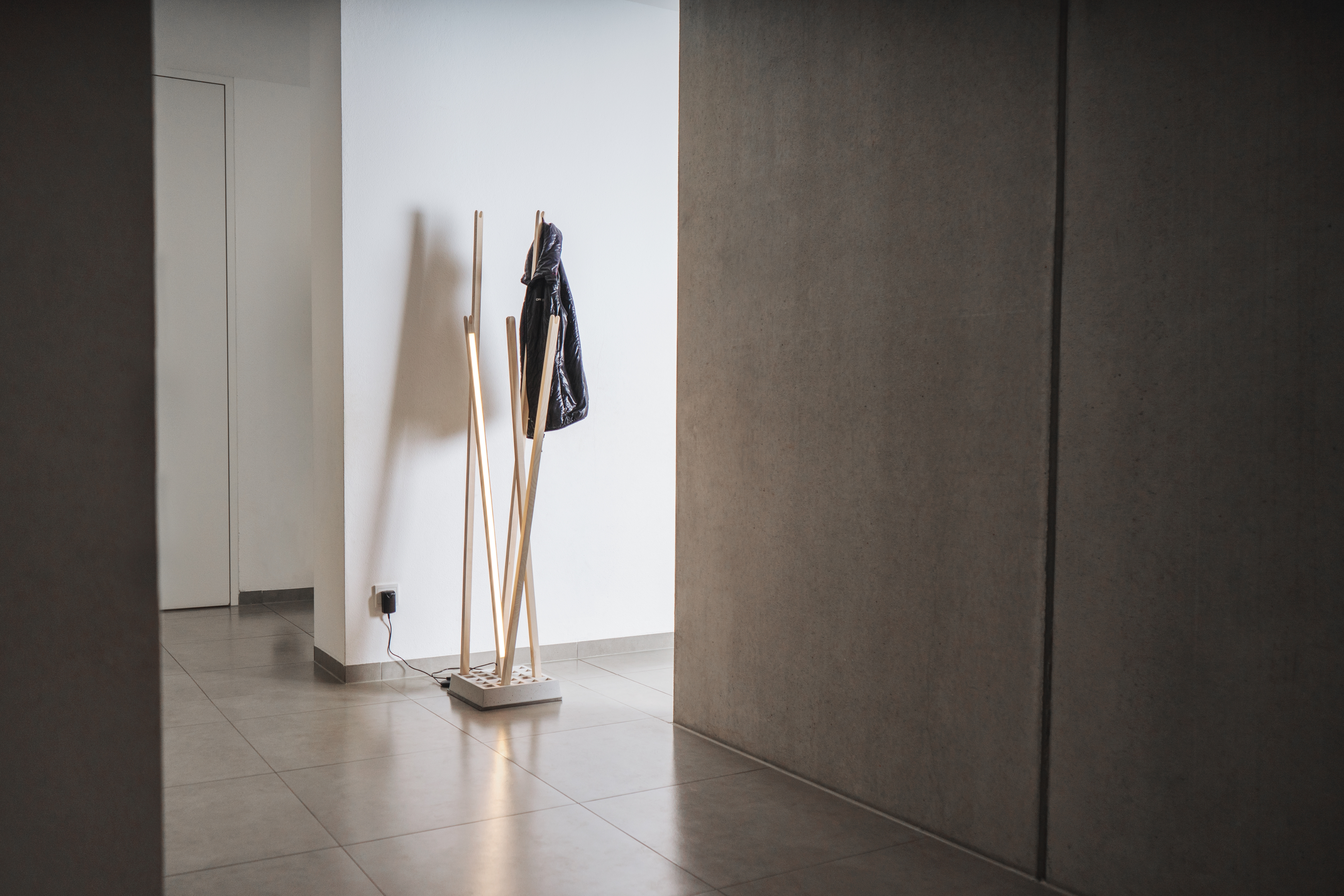 Nils Holger Moormann Pin Coat Garderobe mit Pin Light Leuchte und schwarzer Jacke im Flur.