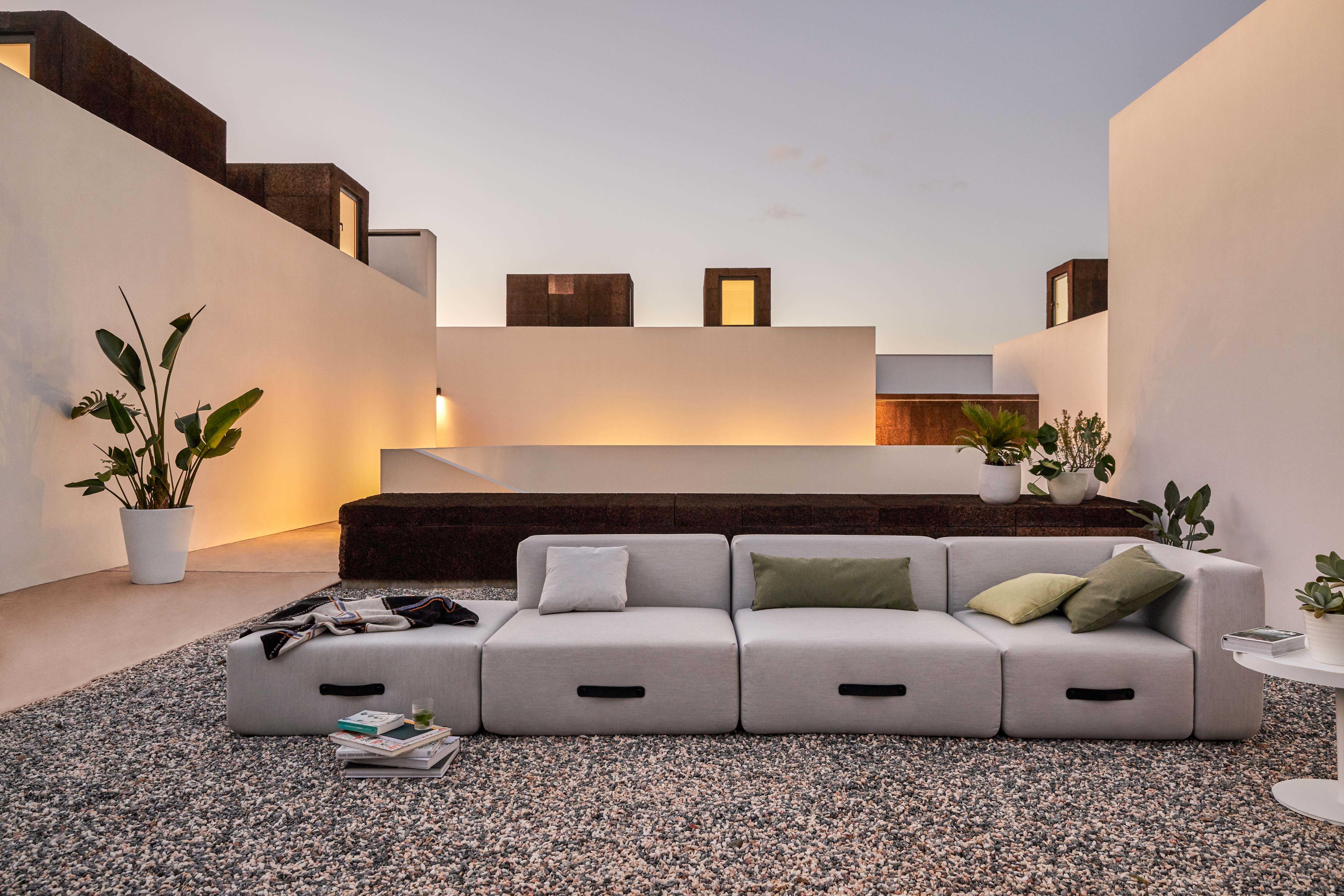 Miami Outdoor Sofa von Conmoto mit Hocker auf Kiesterrasse, minimalistisches Design mit Pflanzen.