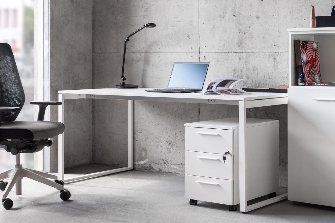Weißer Frezza Pop Square Schreibtisch mit Rollcontainer, Lampe und Laptop vor einer Betonwand.