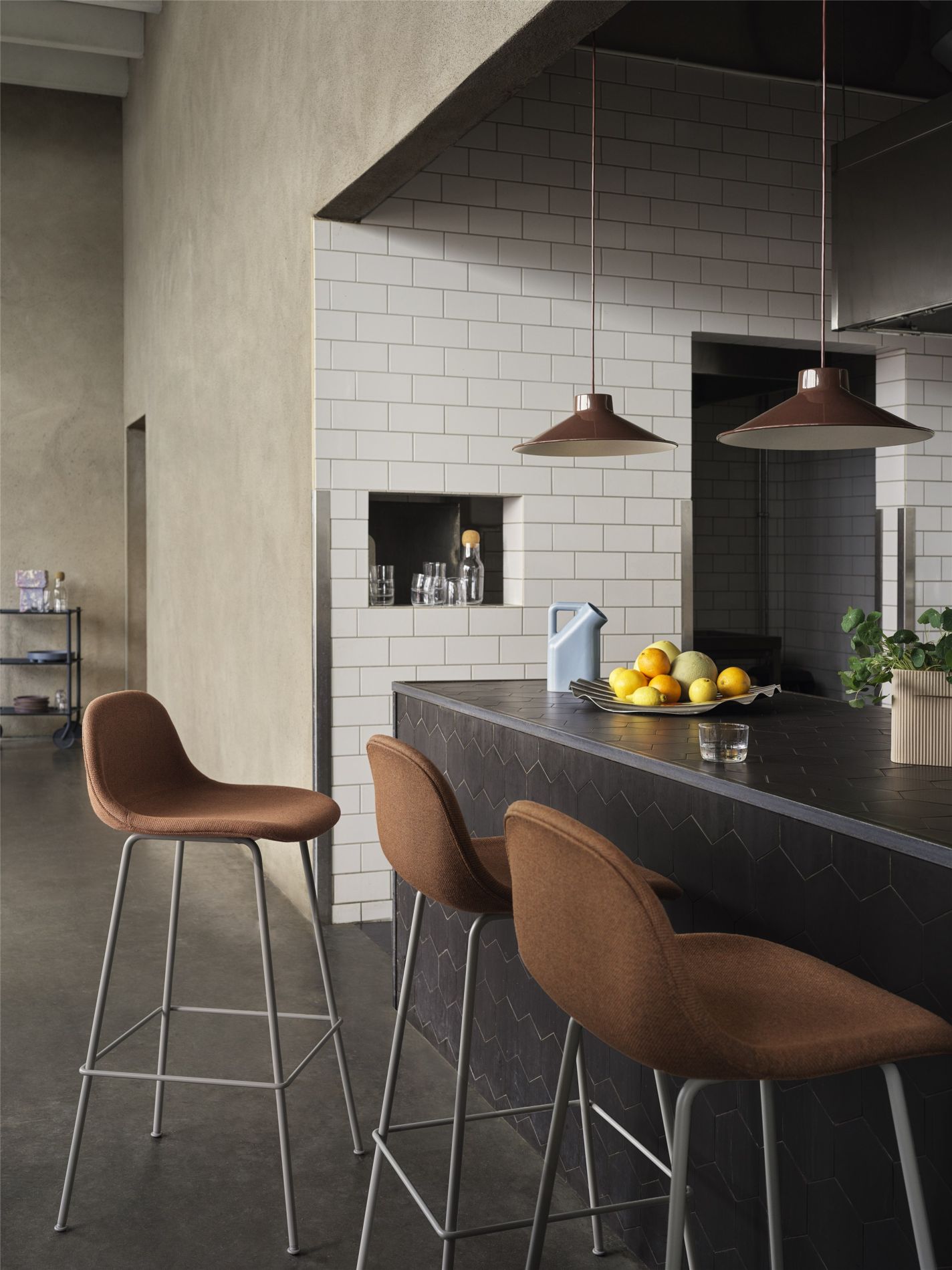 Braune Barhocker mit grauen Metallbeinen an einer Kücheninsel mit Obst und Pendelleuchten.