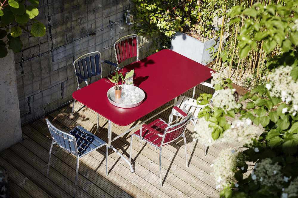 Feuerroter Haefeli Sessel und passender Gartentisch von Embru auf einer sonnigen Terrasse mit Pflanzen.