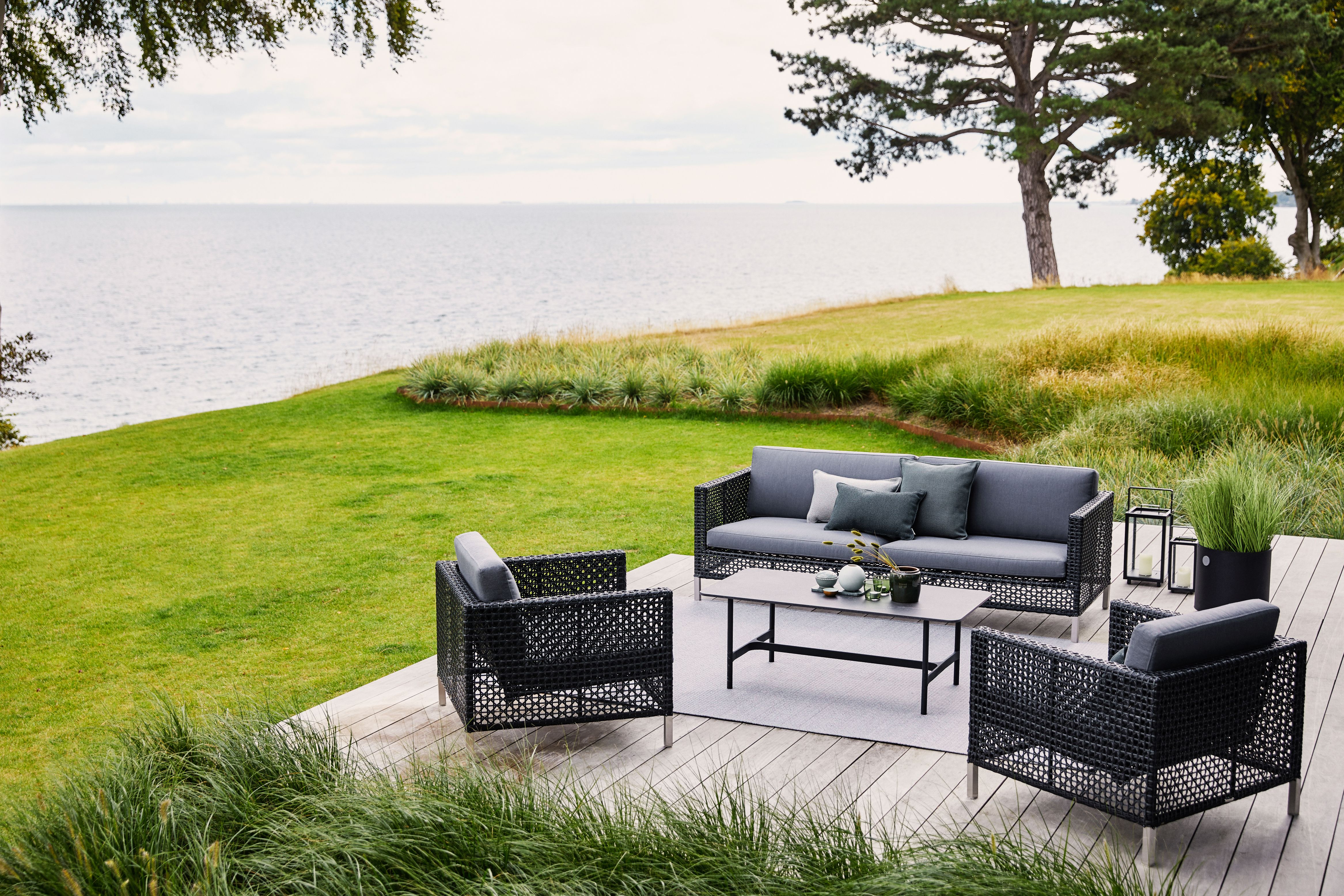 Dot Outdoor Teppich von Cane-Line unter Lounge-Möbeln auf einer Terrasse mit Meerblick.
