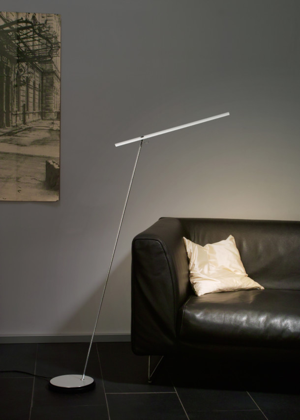 Moderne Stehlampe mit LED-Leuchte in Chromoptik neben schwarzem Ledersofa mit Kissen im Wohnzimmer.