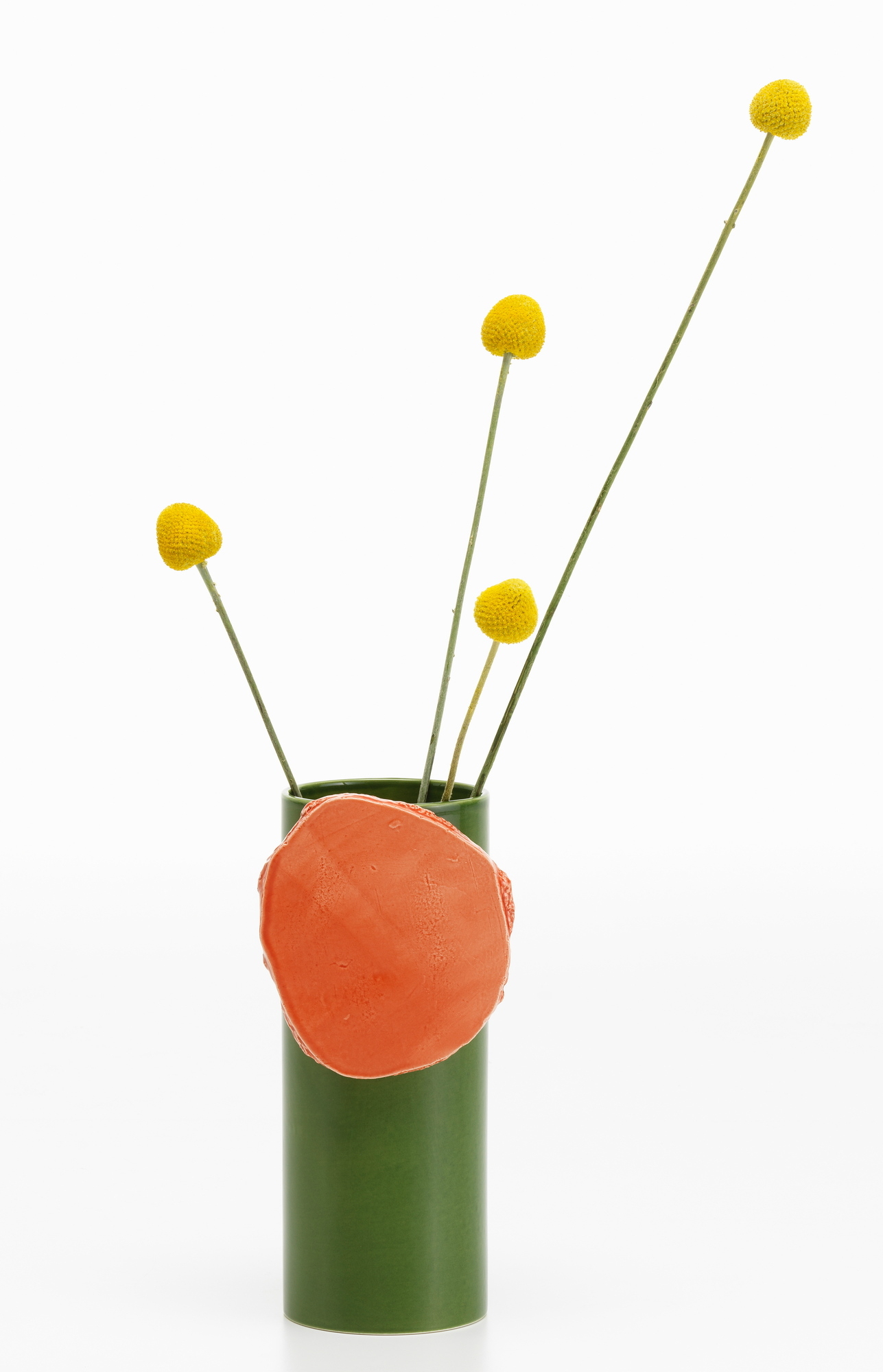 Vitra Découpage Vase: Grüne Design-Vase mit orangefarbenem Dekorelement und gelben Zierblumen auf weißem Hintergrund.