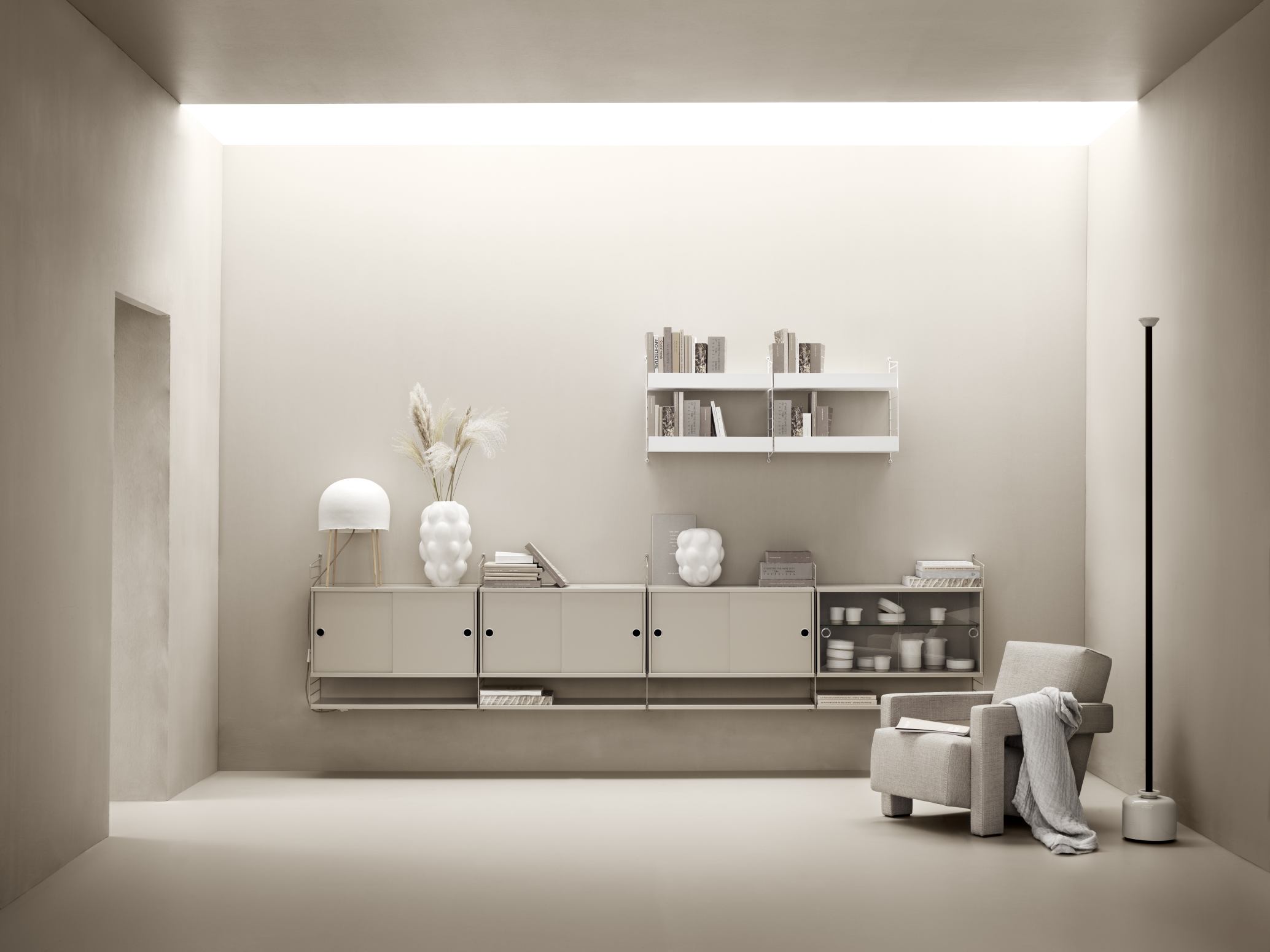 Beige String Regalsystem Wohnzimmer mit Schränken, Regalböden und Sessel. Modernes skandinavisches Design.