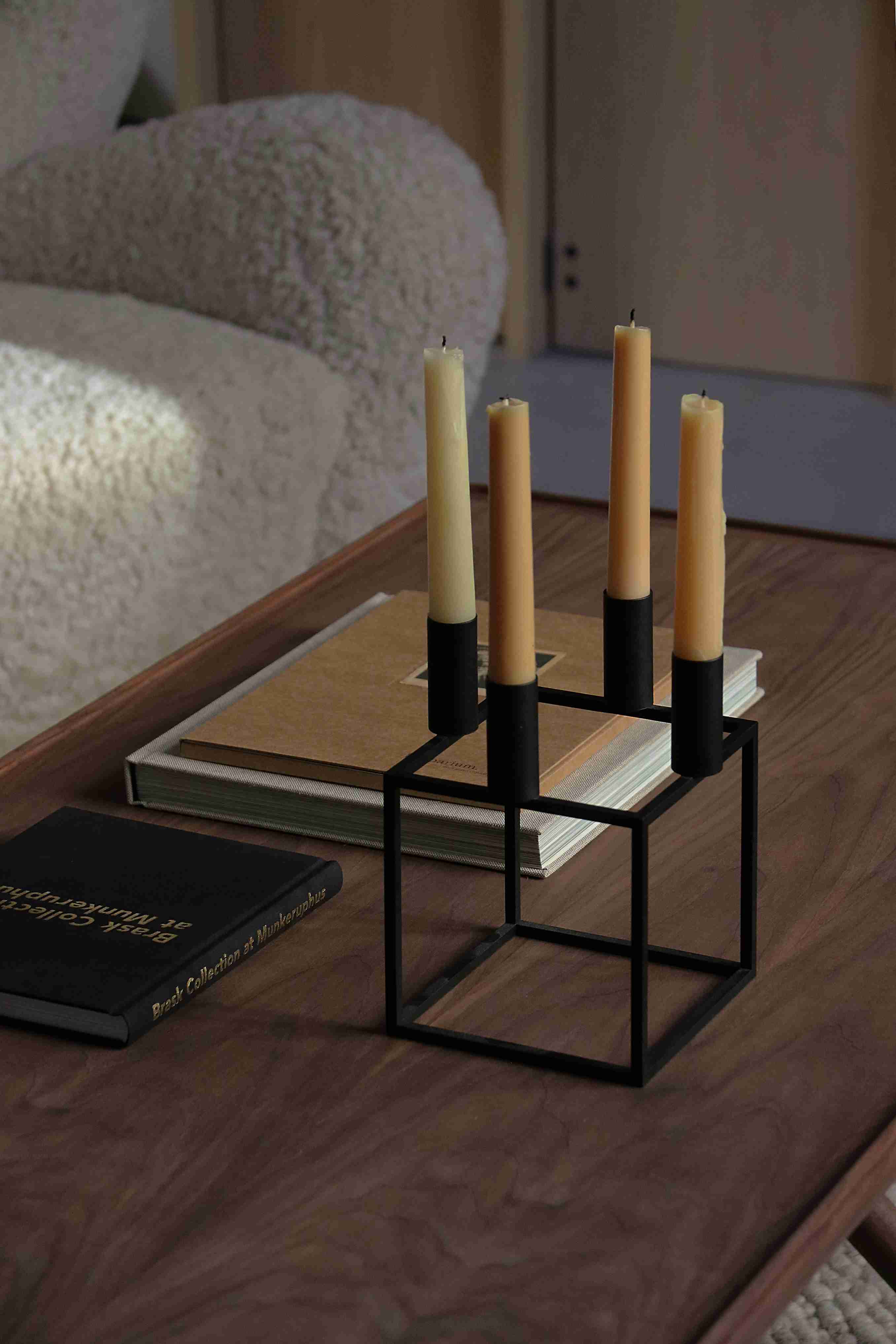 Schwarzer, moderner Kerzenständer aus Metall mit vier beigen Kerzen auf einem Holztisch. Dekorative Wohnaccessoires.