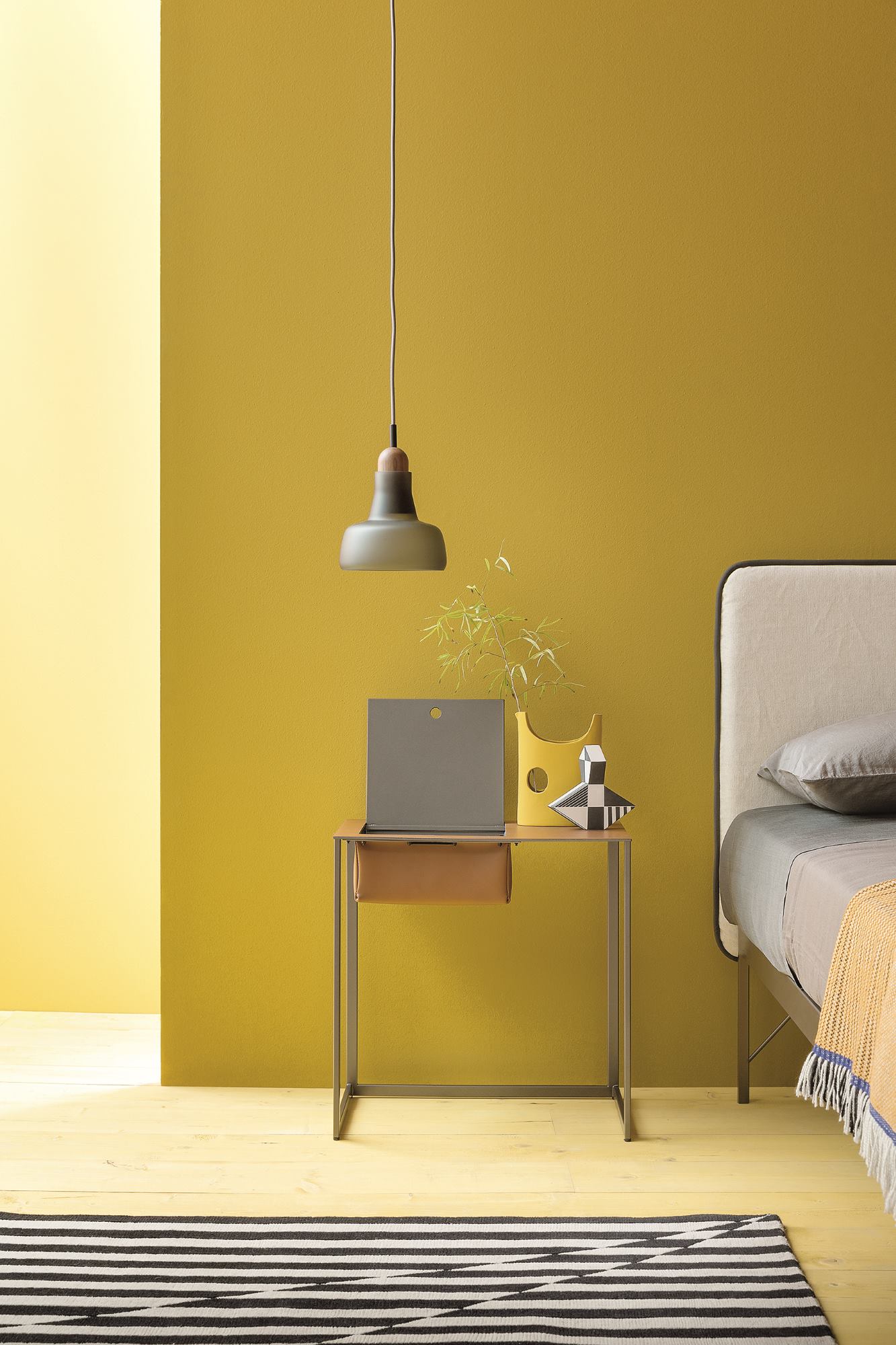 Moderner Taschino Nachttisch von Zanotta mit Schublade, Lampe und Deko-Objekten vor gelber Wand.