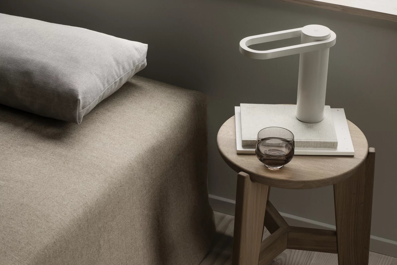 Eli Stool Sitzhocker von Blomus neben Bett mit Lampe und Wasserglas, minimalistisches skandinavisches Design.