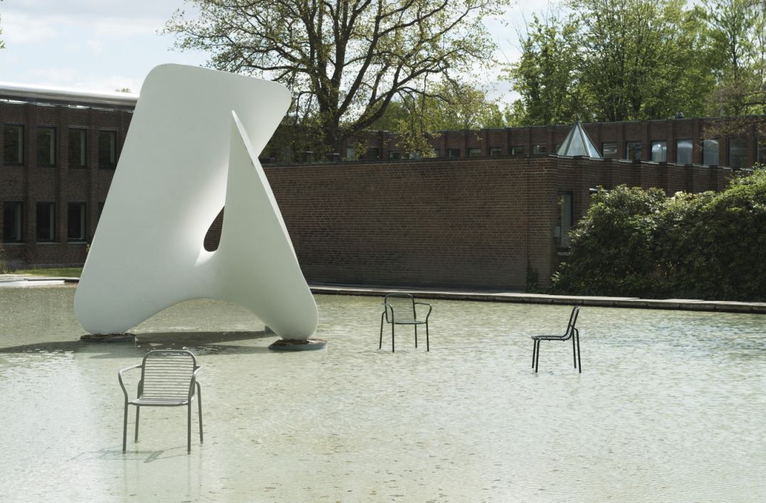 Drei Vig Chair Outdoor Stühle von Normann Copenhagen stehen im Wasser vor einem Gebäude und einer Skulptur.