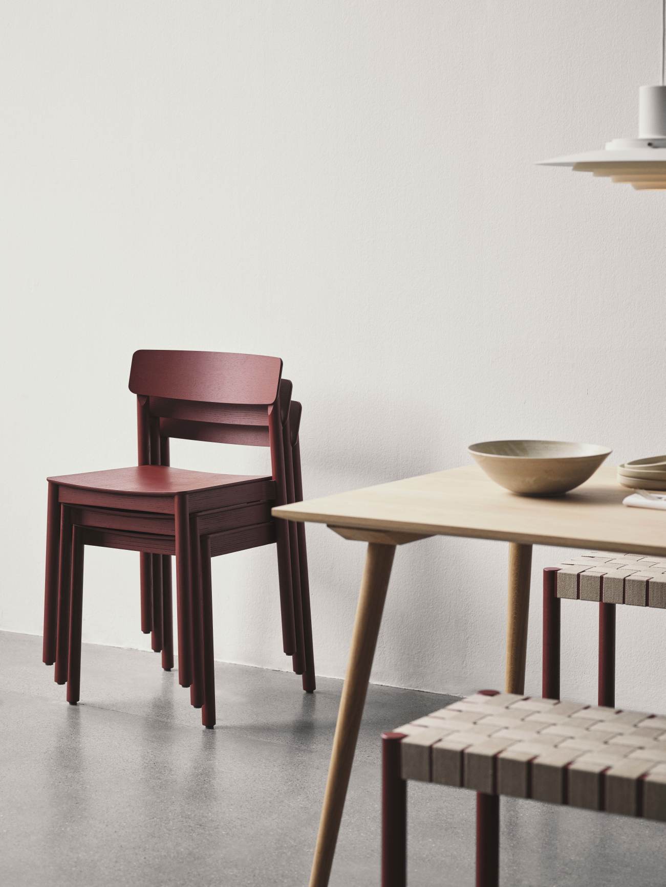 AndTradition In Between Table SK5 mit Holzstühlen in Burgunderrot und passender Bank im minimalistischen Esszimmer.