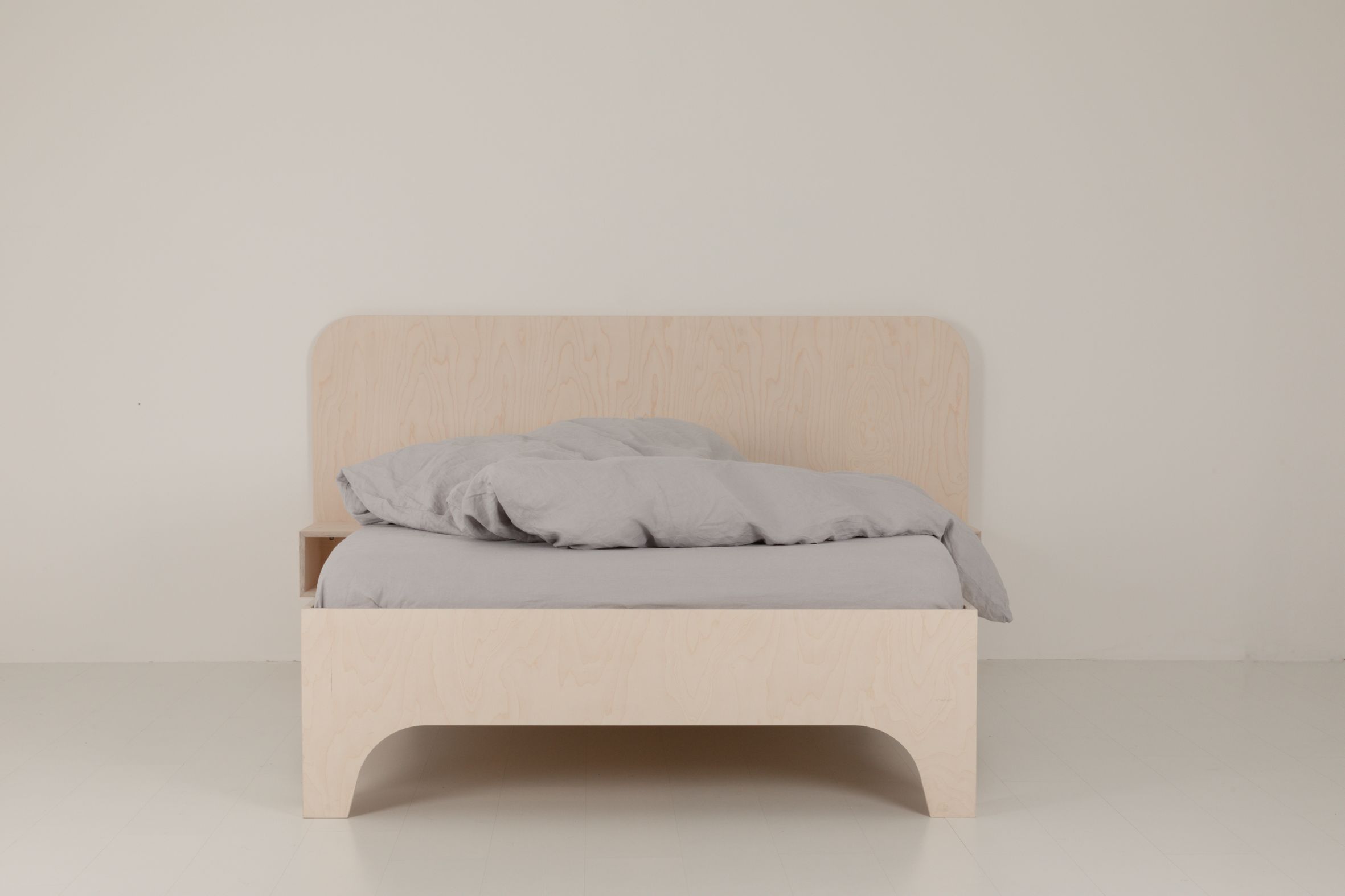 VALENTINA Bett aus hellem Holz mit grauer Bettwäsche und Nachttischablage für ein minimalistisches Schlafzimmer.
