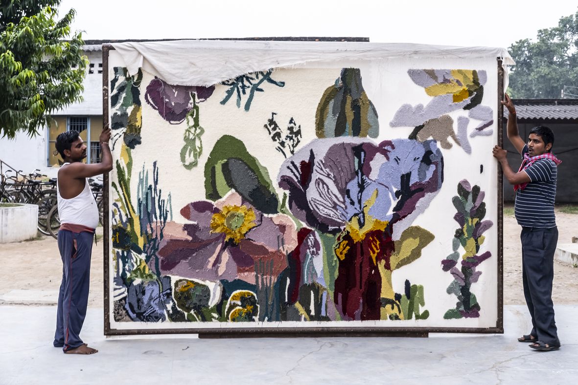 Handgefertigter Nanimarquina Teppich "Flora Backyard" mit floralem Muster, gehalten von zwei Personen.