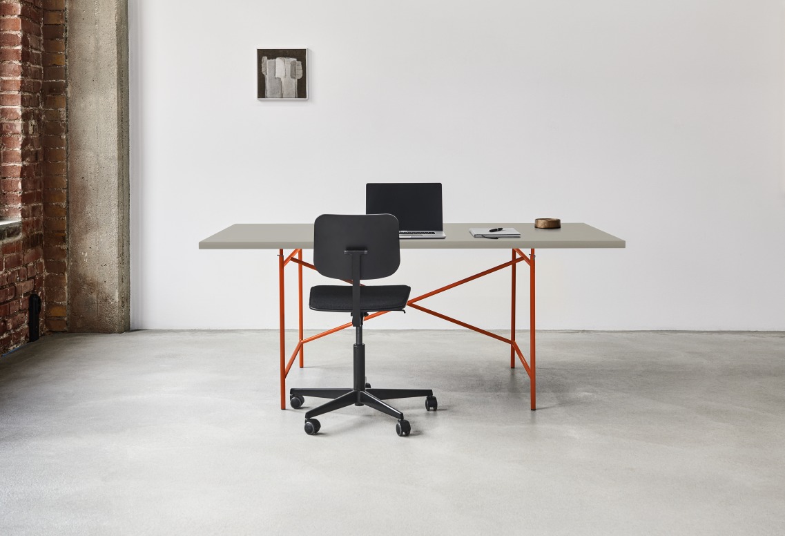 Eiermann Tisch mit orangefarbenem Gestell, grauer Tischplatte, Bürostuhl, Laptop und Notizbuch in modernem Büro.