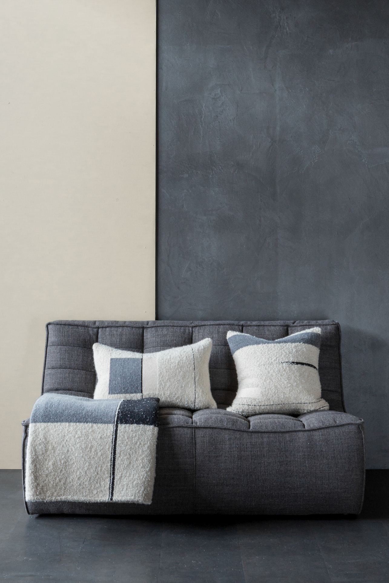 Urban Überwurf Ethnicraft: Graues Sofa mit Kissen und Decke im modernen Wohnzimmer, Textilien in Grau- und Weißtönen.