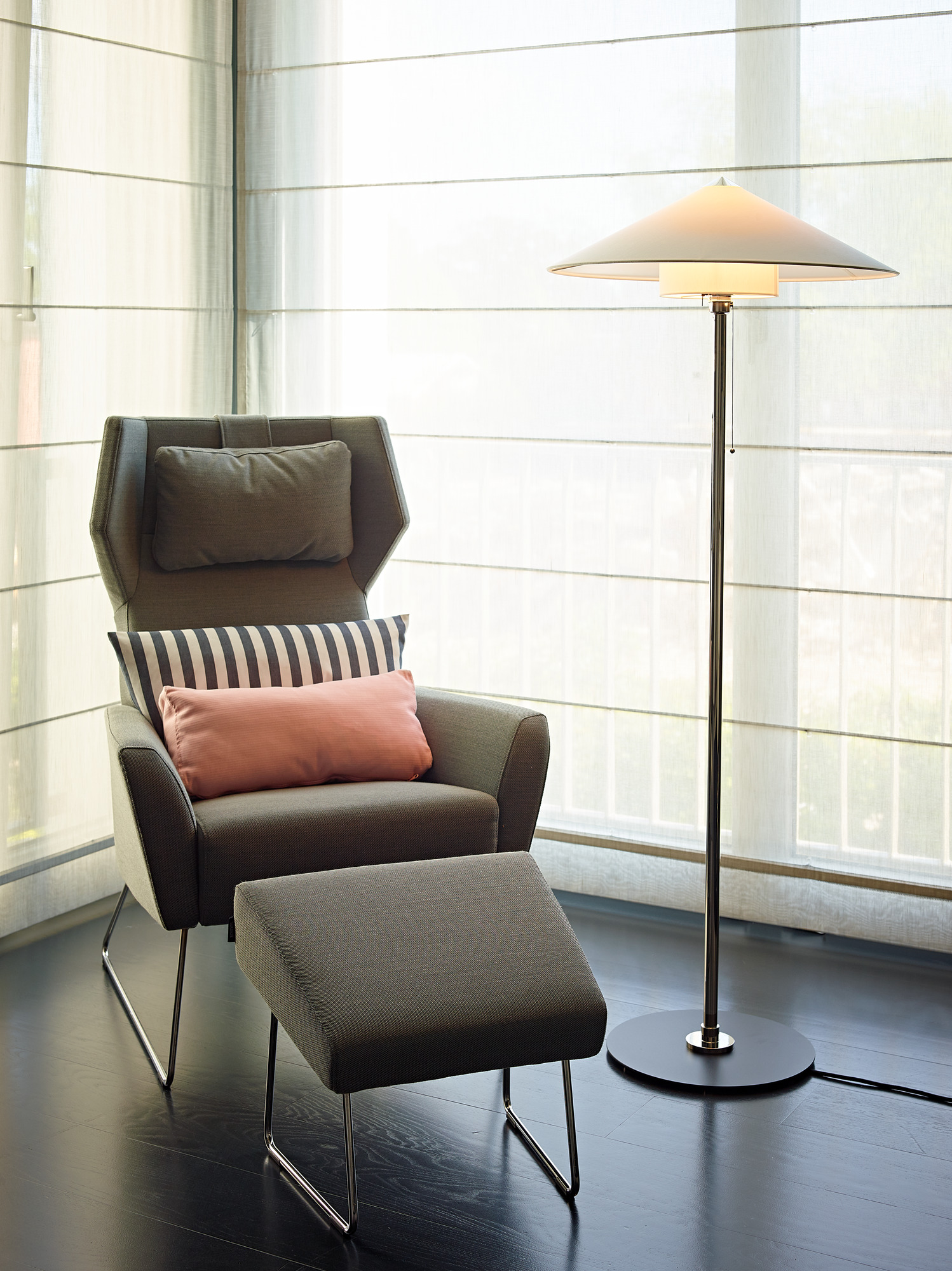 Tecnolumen Wagenfeld Stehleuchte WST L 30 neben Sessel mit Fußhocker, modernes Wohnzimmerambiente mit Designklassiker.