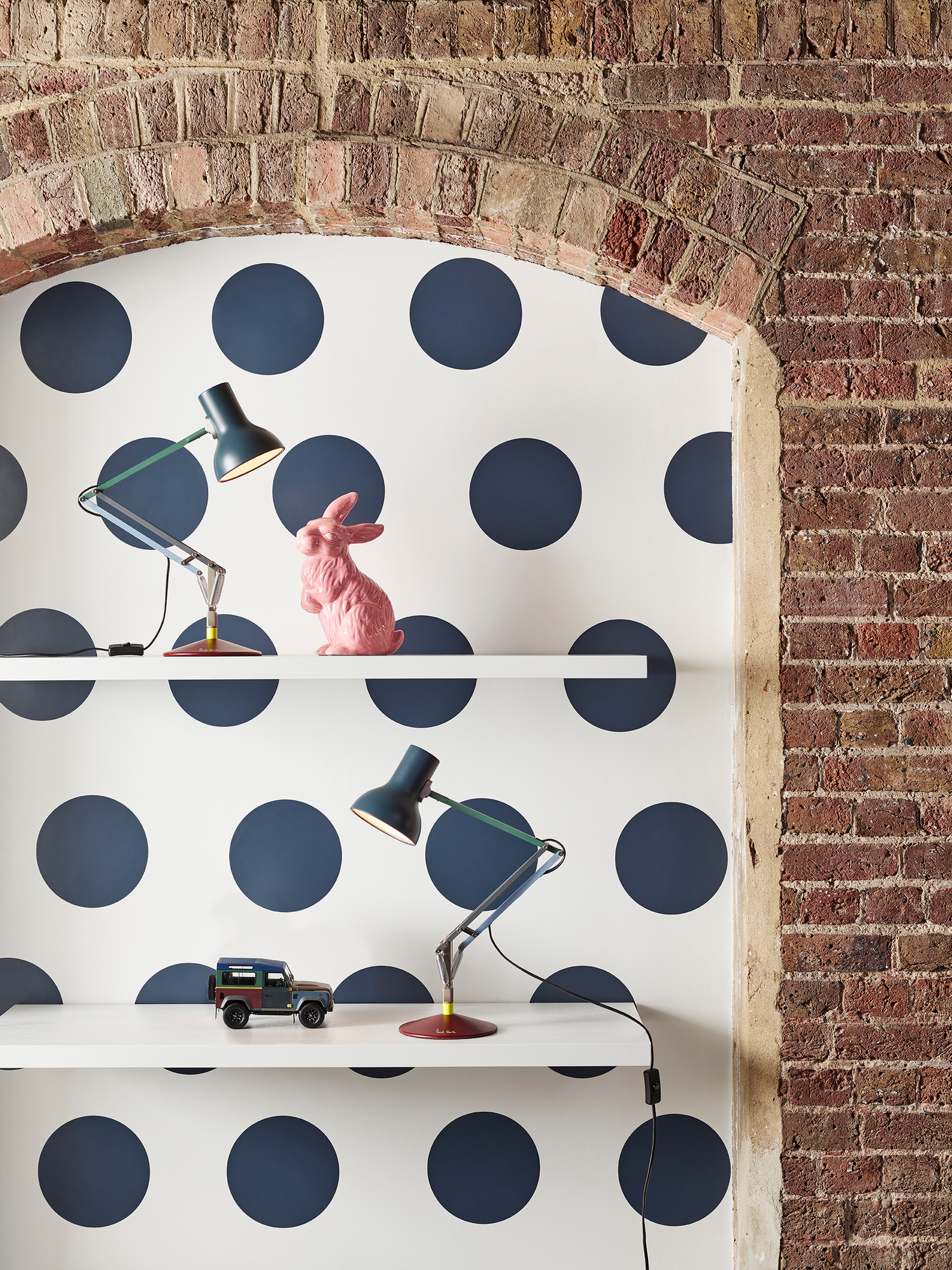 Type 75 Mini Anglepoise Tischleuchte Paul Smith Edition auf Regal mit Deko-Objekten vor Punktmuster-Tapete.