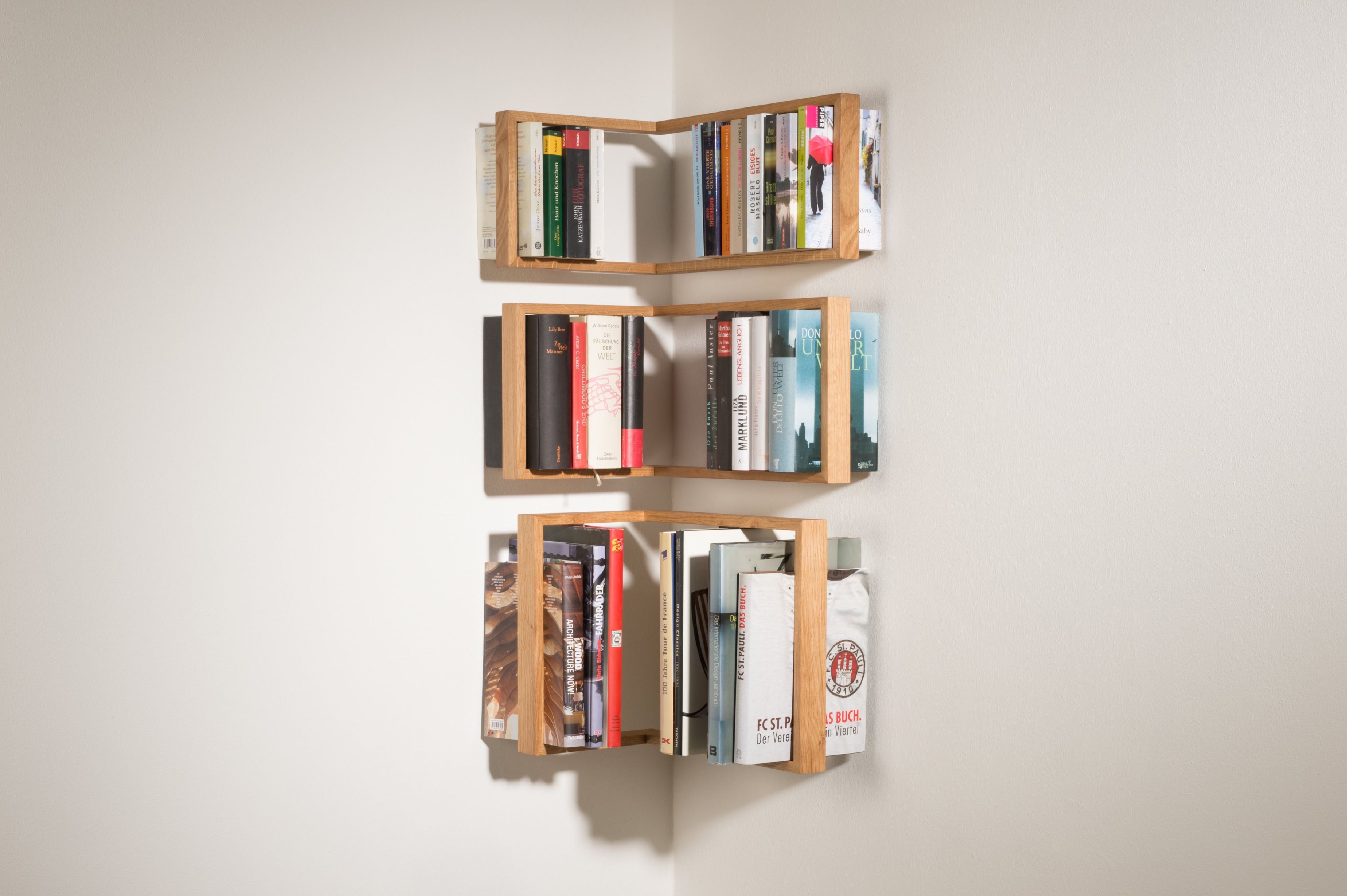 Eiche Regal b-eck, das kleine b, dreifach übereinander an einer weißen Ecke montiert und mit Büchern gefüllt.