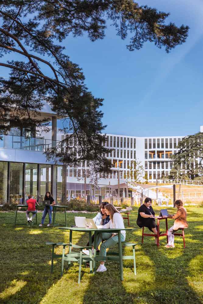 Personen sitzen auf Fermob Hockern im Freien und arbeiten an Laptops. Outdoor Möbel.