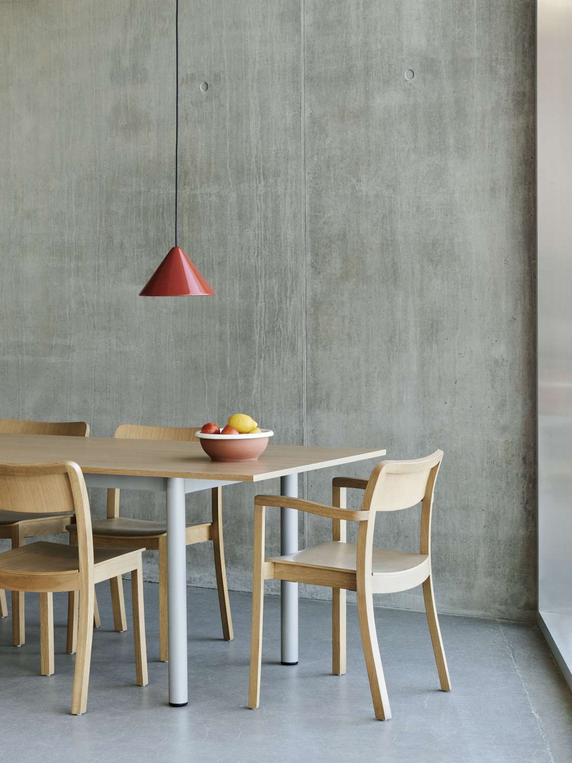 Annex Table Overhang Esstisch von Hay mit Holzstühlen und roter Lampe vor einer Betonwand.