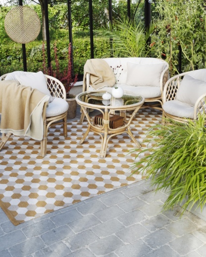 Beige-weißer Outdoor-Teppich mit geometrischem Muster unter Rattanmöbeln im Wintergarten. Gartenmöbel und Dekoration.