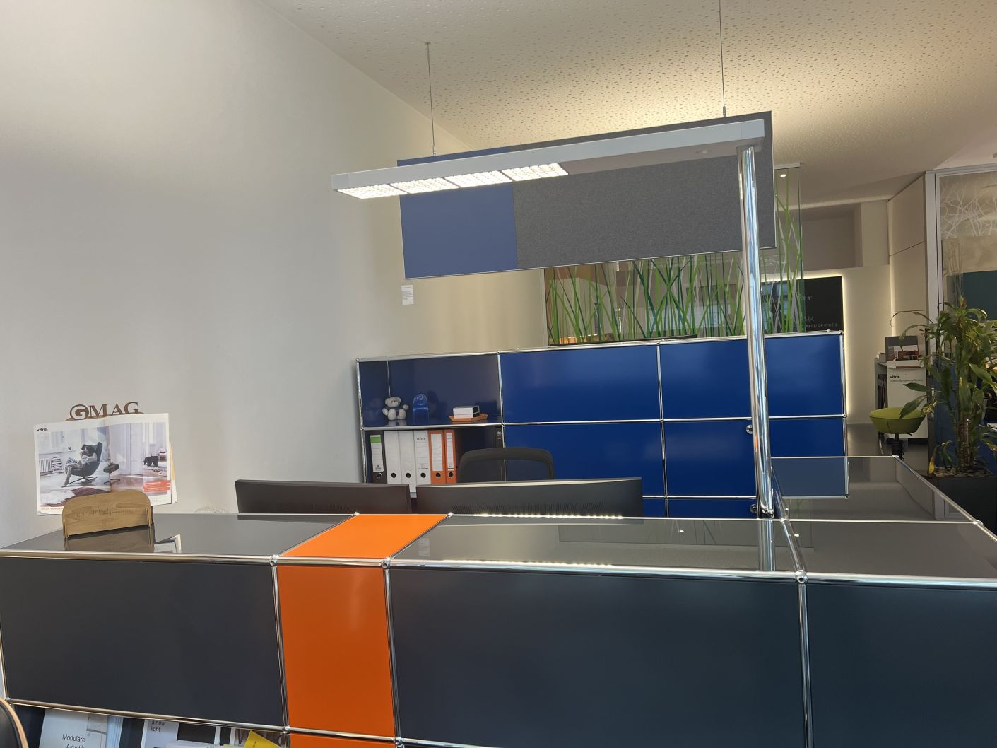 USM Haller Theke in Anthrazit und Orange, gebrauchtes modulares Empfangsmöbel mit blauen Regalen im Hintergrund.