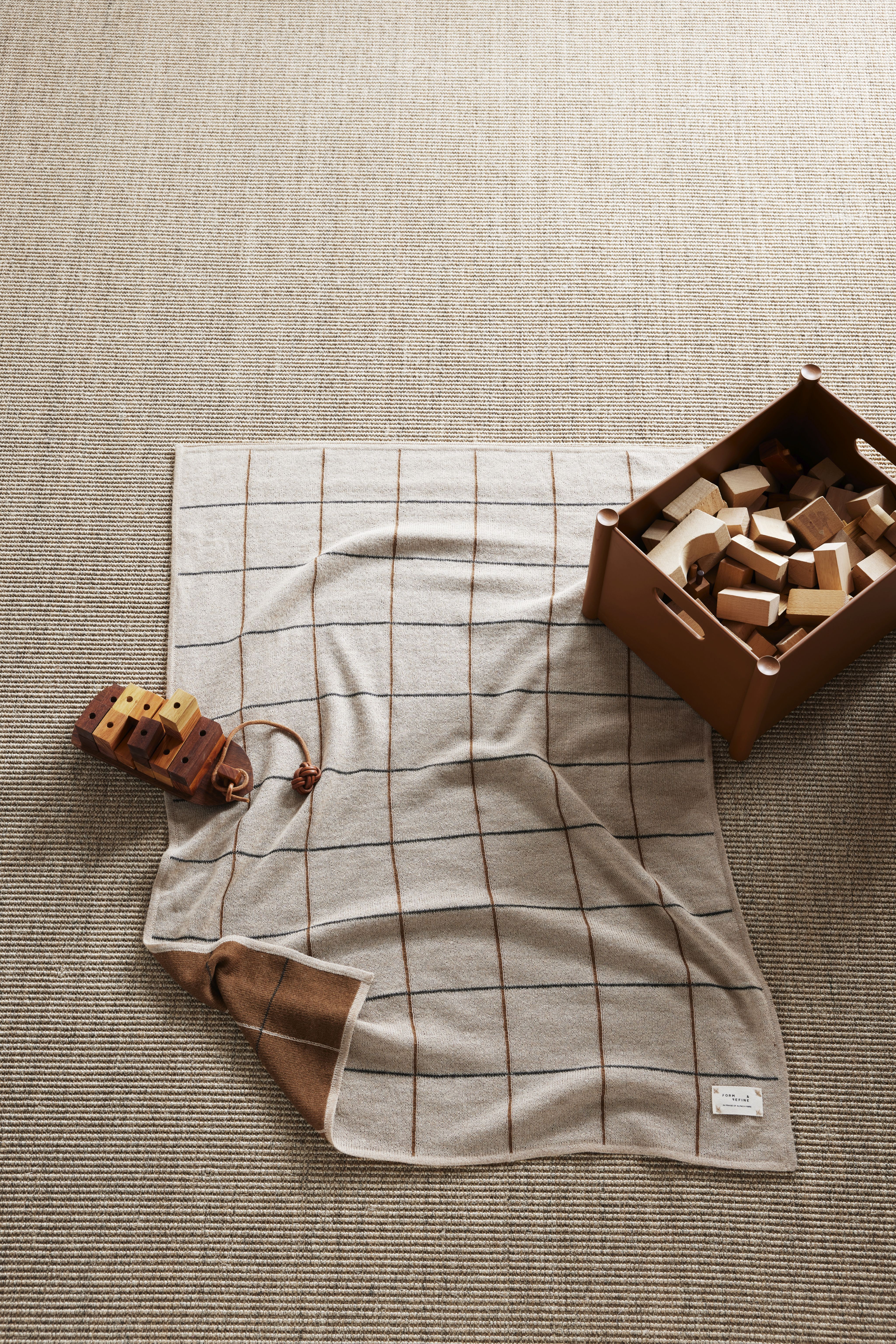 Plaiddecke "Form & Refine" mit Holzspielzeug und Bauklötzen für Kinder auf einem Teppich.