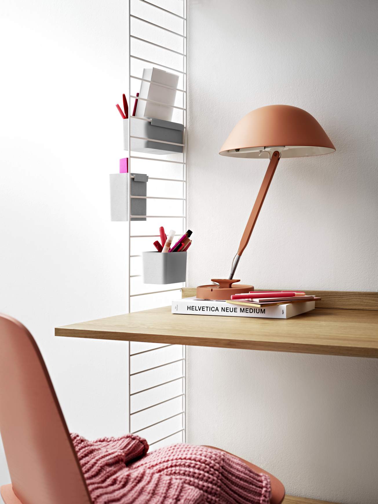 Arbeitsplatz mit String Furniture Regalsystem, Schreibtisch, Lampe und Ablagefächern für Bürobedarf.