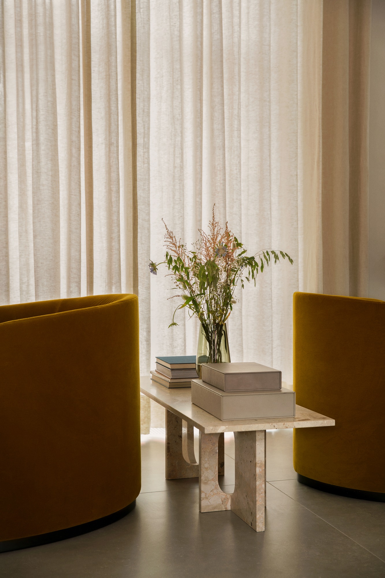 Androgyne Couchtisch von Audo Copenhagen aus Travertin mit Dekoration und gelben Sesseln im Wohnzimmer.