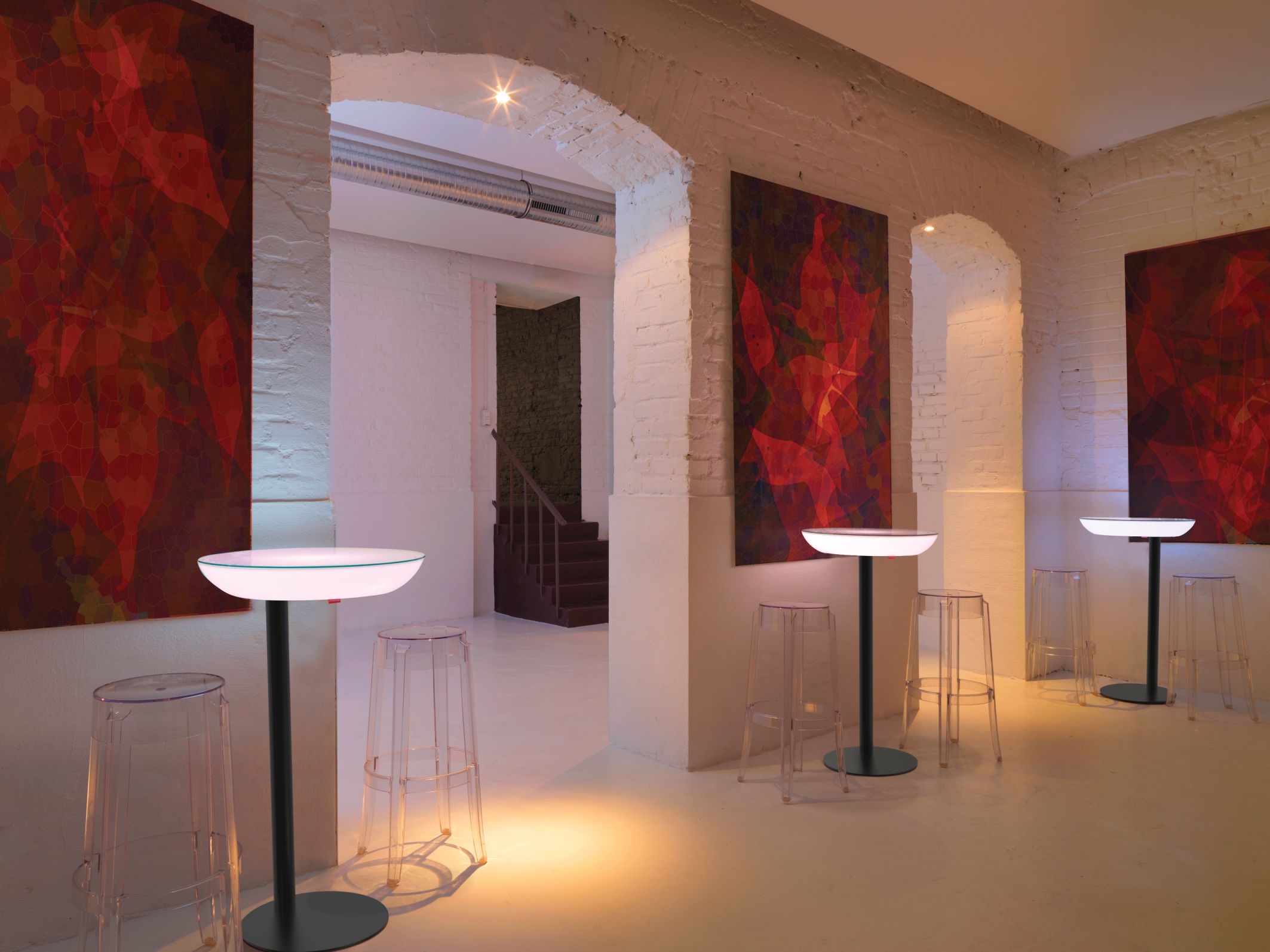 Mehrere Moree Lounge M105 Leuchttische mit transparenten Barhockern in einem modernen, hellen Raum.