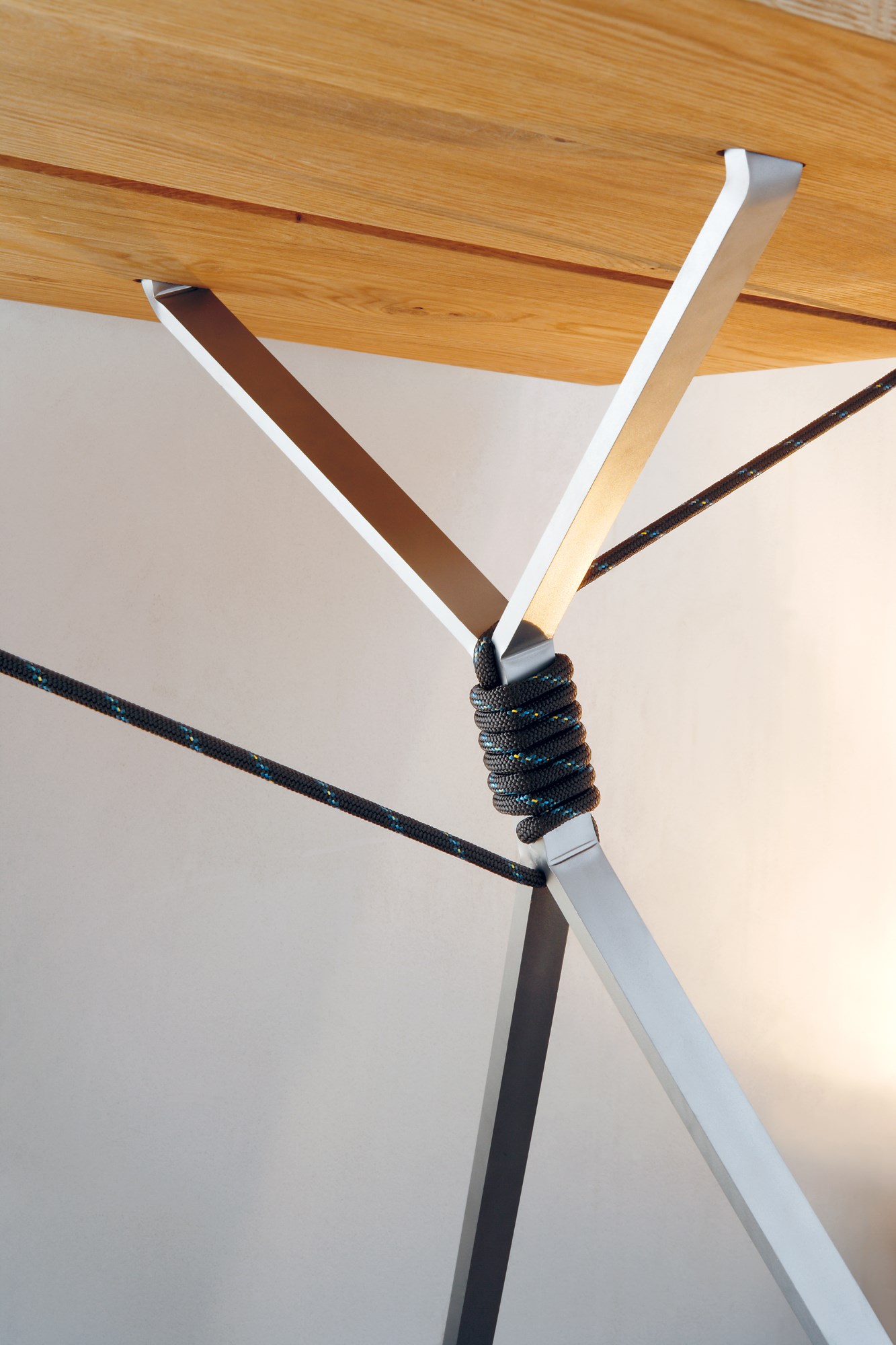 Detailaufnahme Kampenwand Tisch von Nils Holger Moormann: Tischbein aus Metall mit Seilwicklung unter einer hellen Holzplatte.