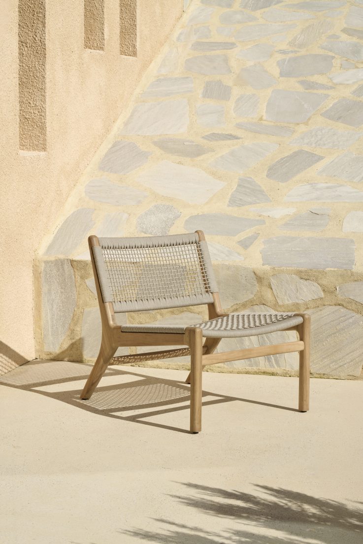Jack Loungesessel von Ethnicraft: Teakholz Outdoor Sessel mit beige Kordelgeflecht vor einer Steinwand.