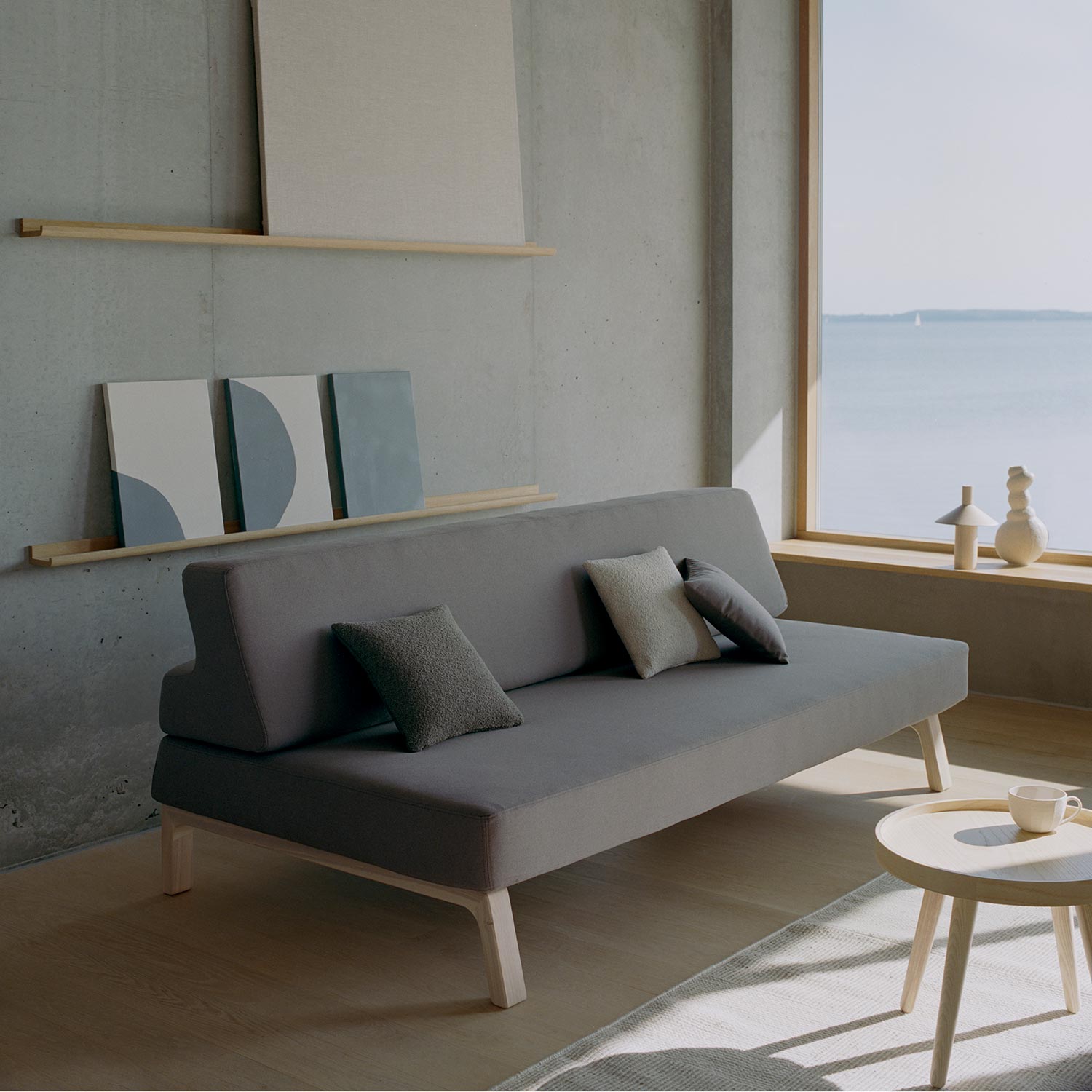 Graues Schlafsofa mit Kissen im modernen Wohnzimmer mit Meerblick, minimalistisches Design und hellem Holztisch.