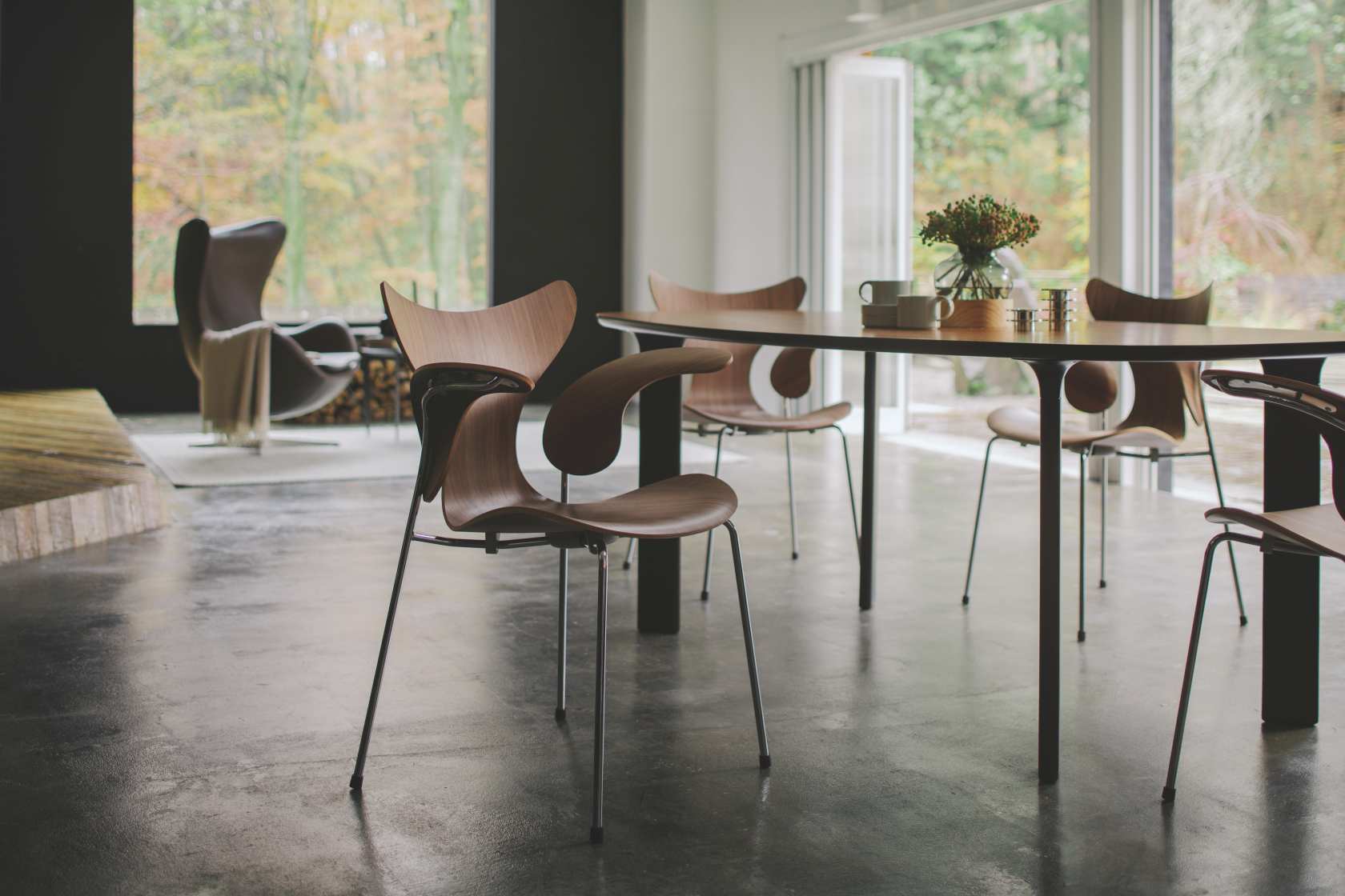 Fritz Hansen Lily Armlehnenstuhl 3208 aus Holz mit Stahlbeinen am Esstisch im modernen Wohnzimmer.