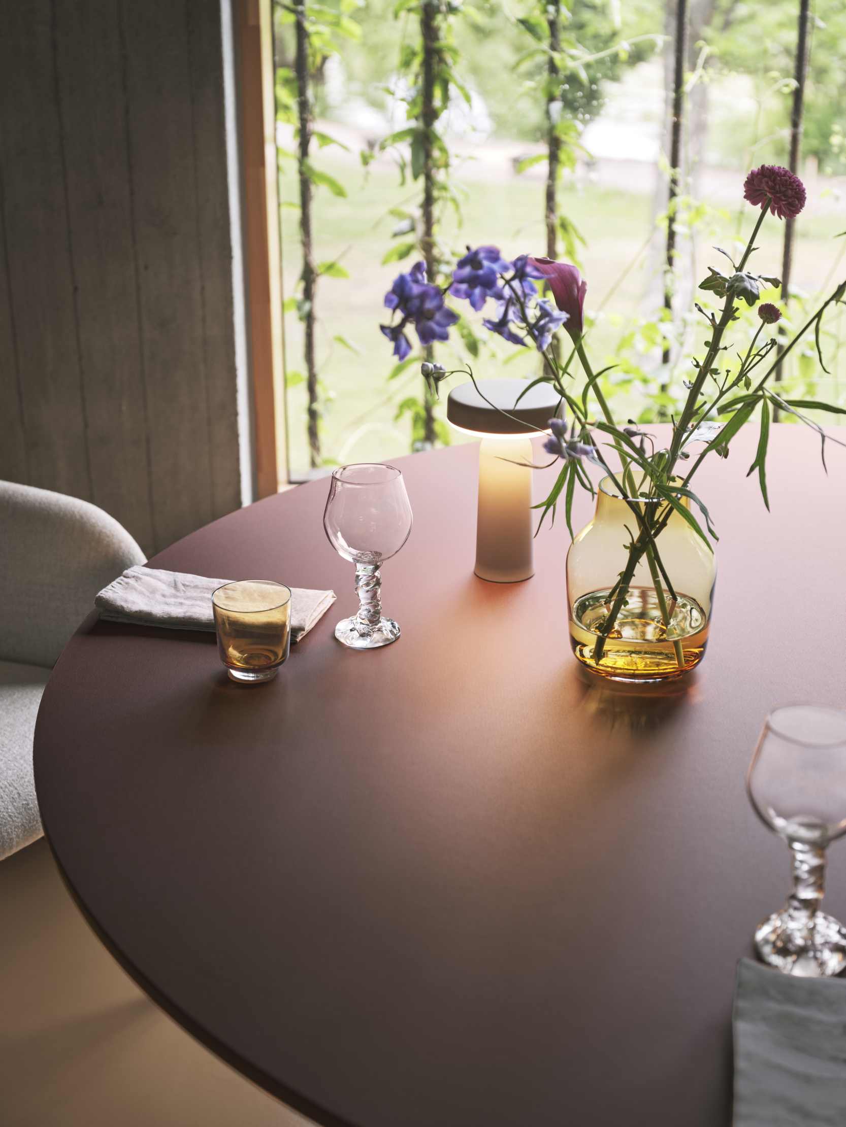 Nahaufnahme eines Muuto Fiber Soft Armchair Stuhls an einem Esstisch mit Blumen, Gläsern und Lampe.