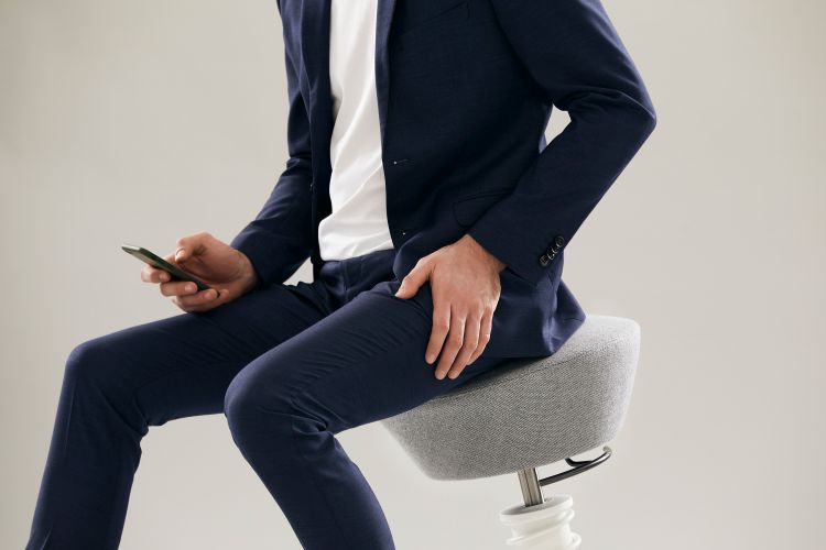 Mann sitzt auf einem grauen Swopper Hocker mit Rollen und benutzt ein Smartphone.