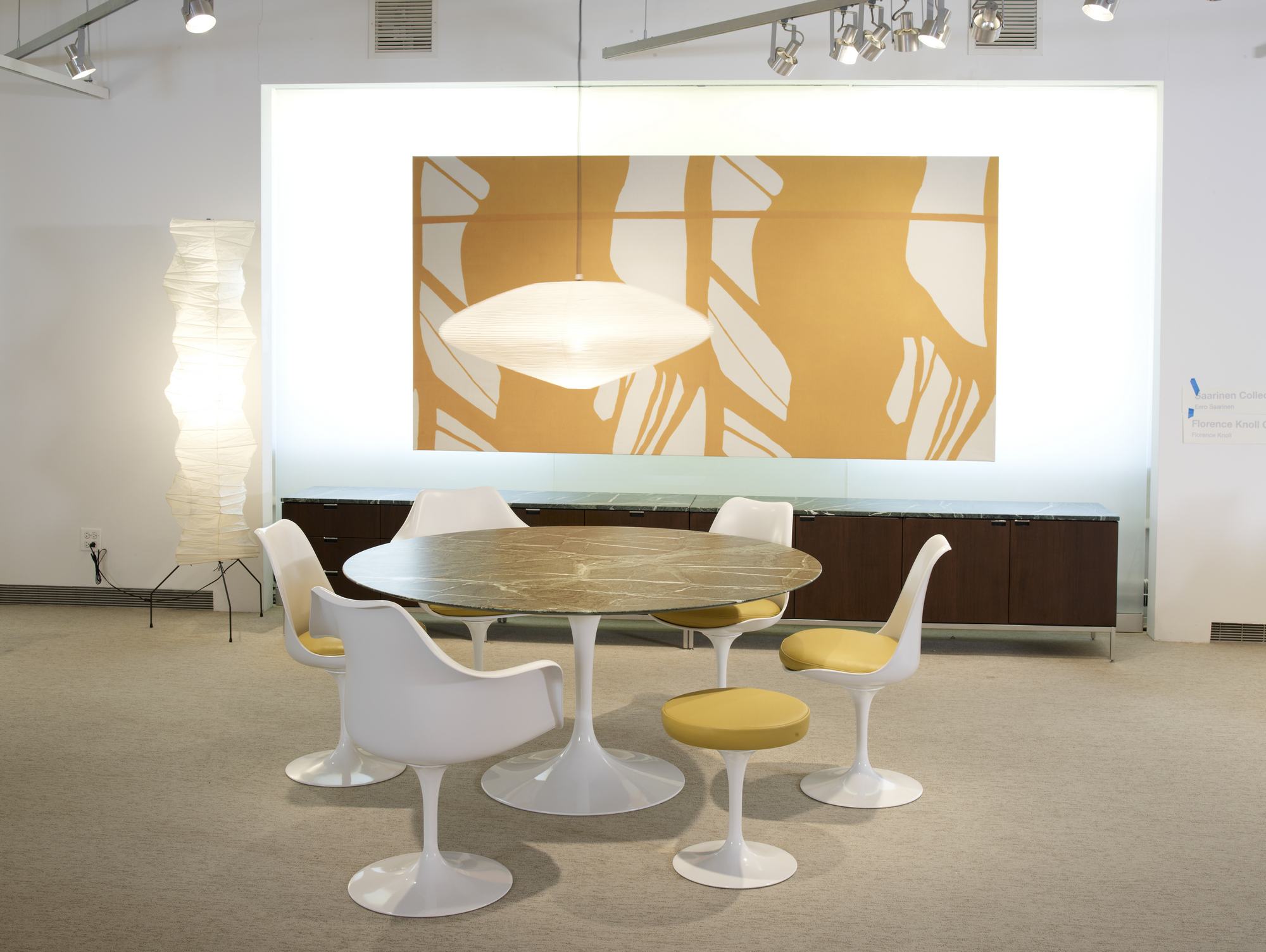 Esszimmer mit rundem Tisch und weißen Tulip Armlehnstühlen von Knoll International mit gelben Sitzpolstern.