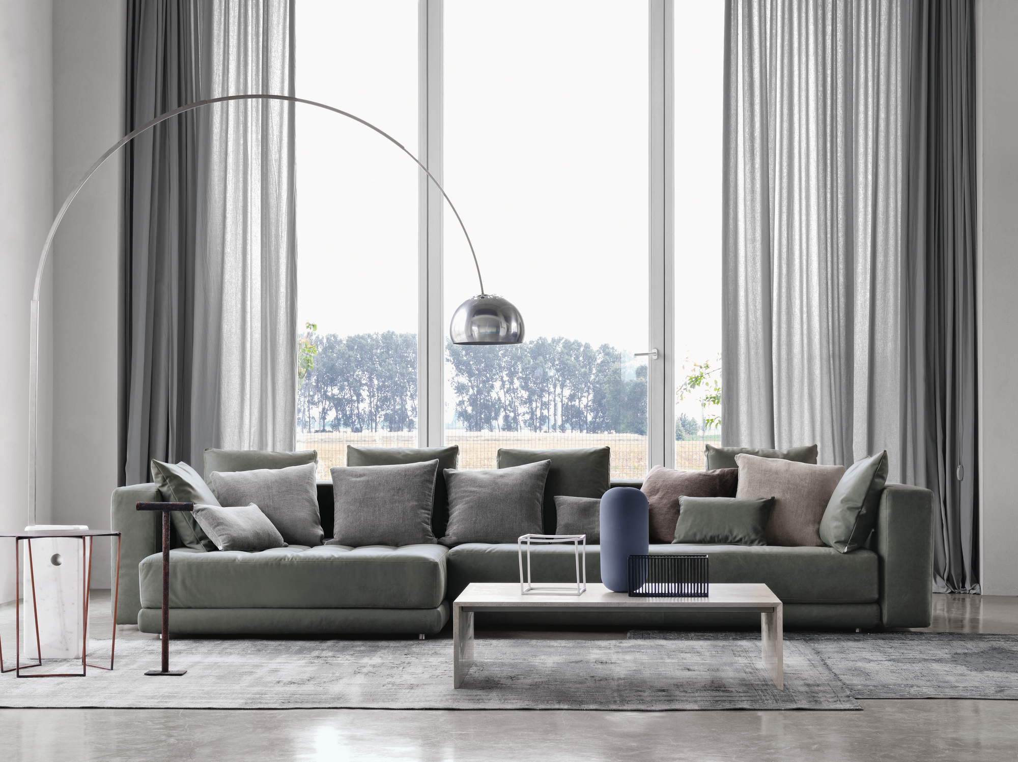Helle Wohnzimmer-Szene mit Flos Arco Stehleuchte, grauem Sofa und großem Fenster.