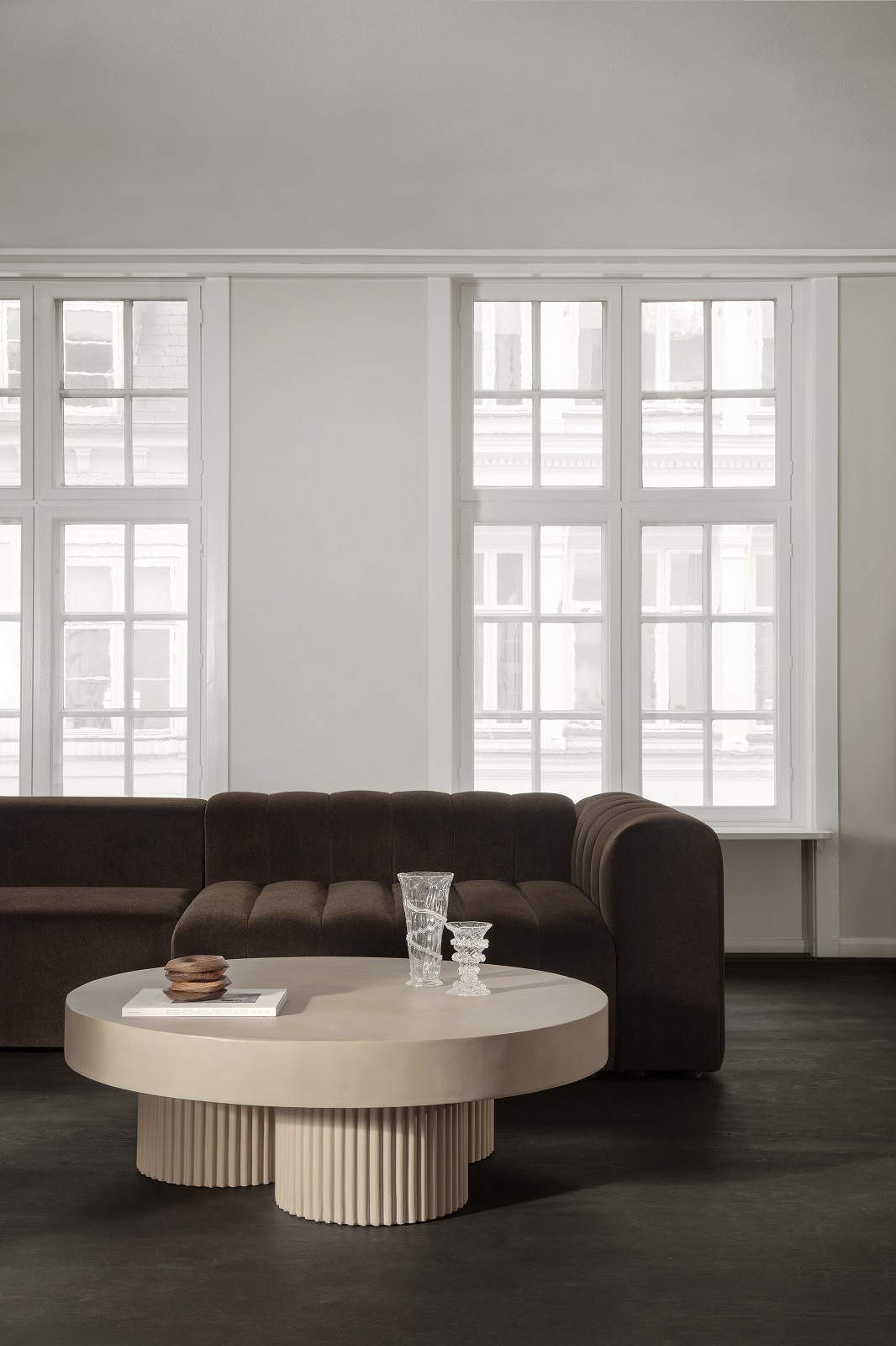 Gear Round Couchtisch von Norr11, runder Wohnzimmertisch aus Beton mit geriffeltem Sockel vor braunem Sofa.
